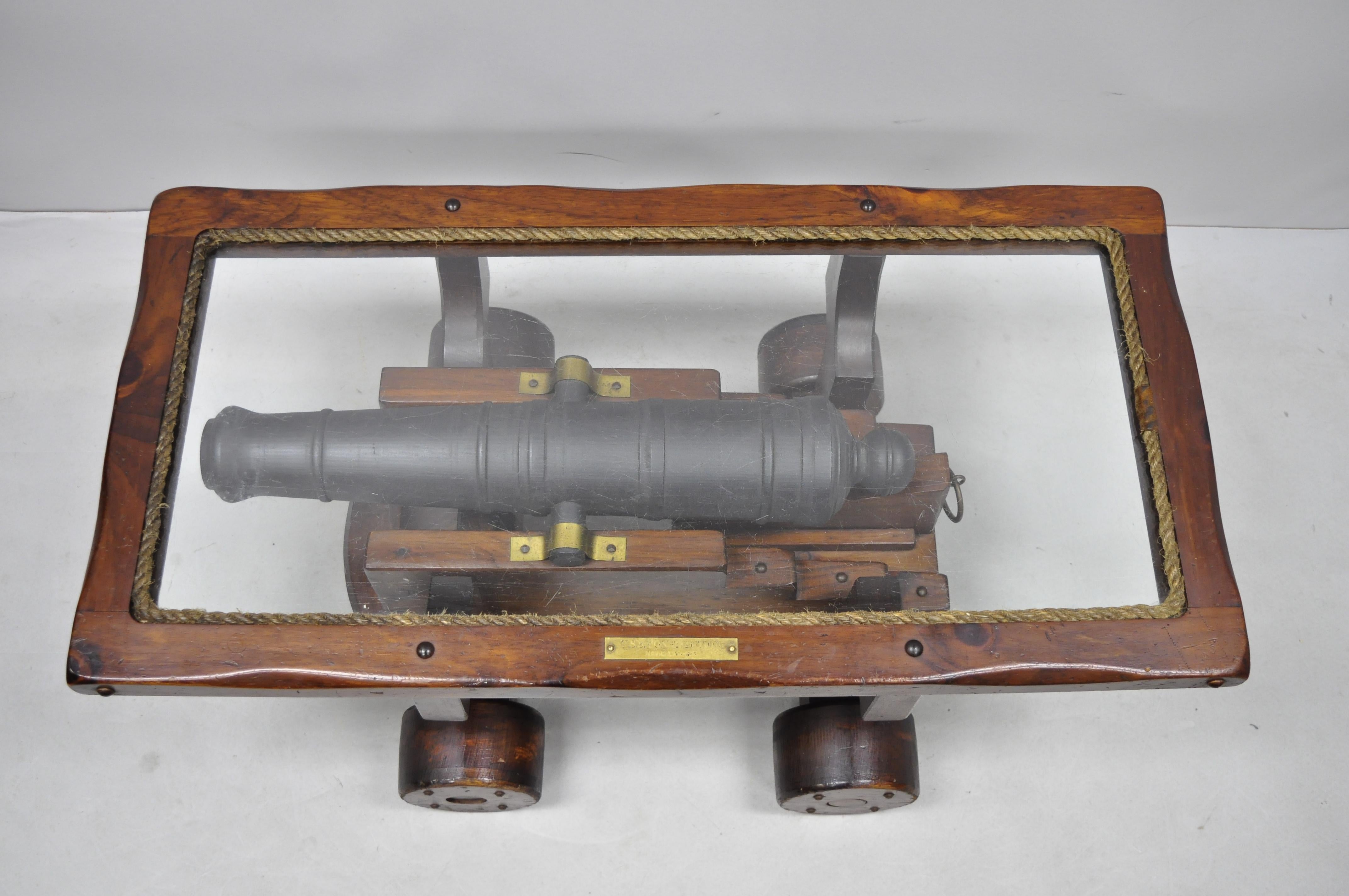 Vintage USS Constitution simulated naval cannon wooden coffee table. Item features carved wood simulated cannon, glass top rope trim, fixed wheels, solid wood construction, beautiful wood grain, distressed finish, brass plaque reads 