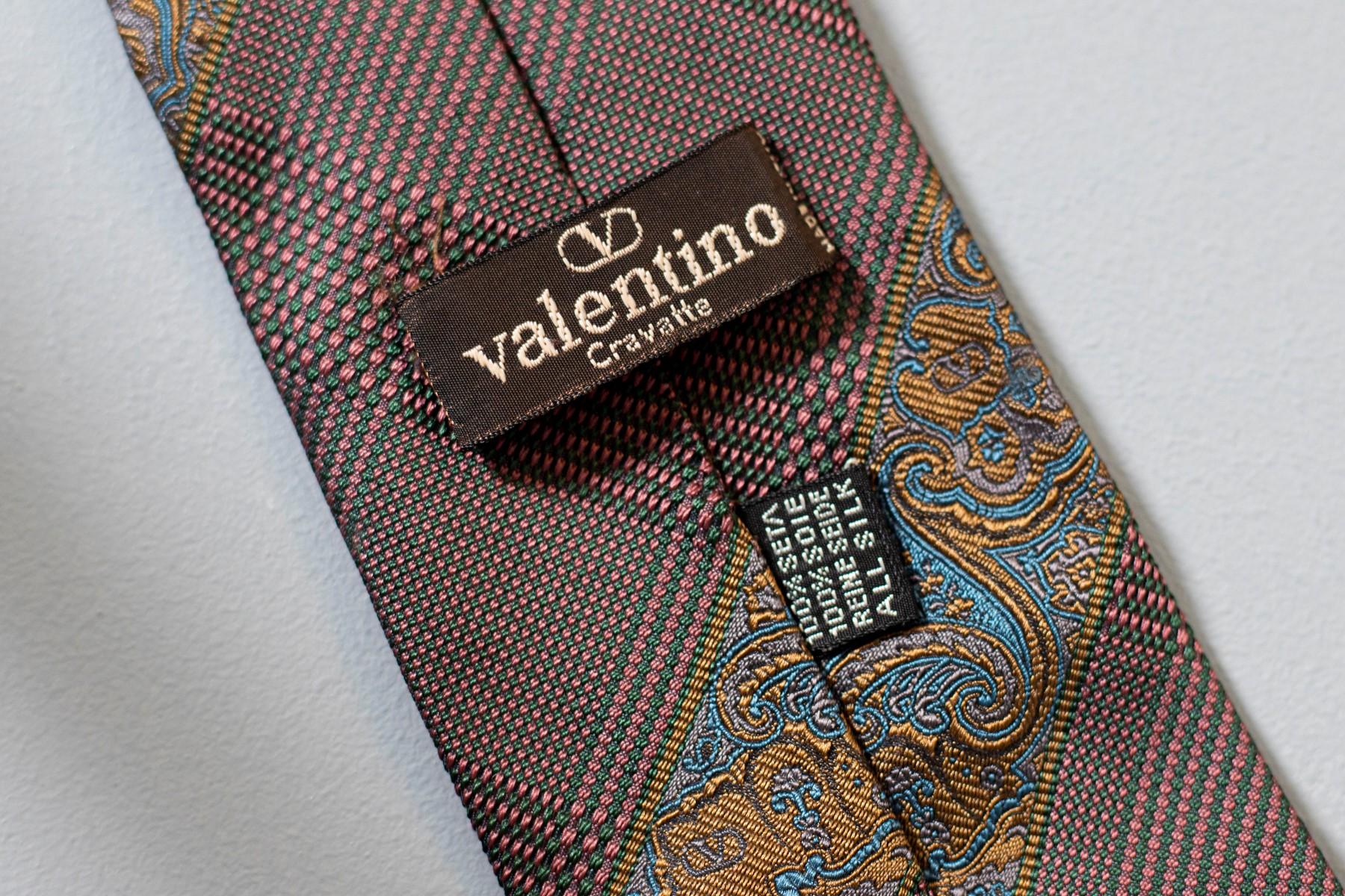 Fabriquée en Italie et conçue par le grand Valentino, cette cravate vintage est classique et élégante. Décorée de motifs dorés et bleus sur un fond brunâtre chaud, cette cravate est idéale pour une soirée formelle et elle se marie parfaitement avec