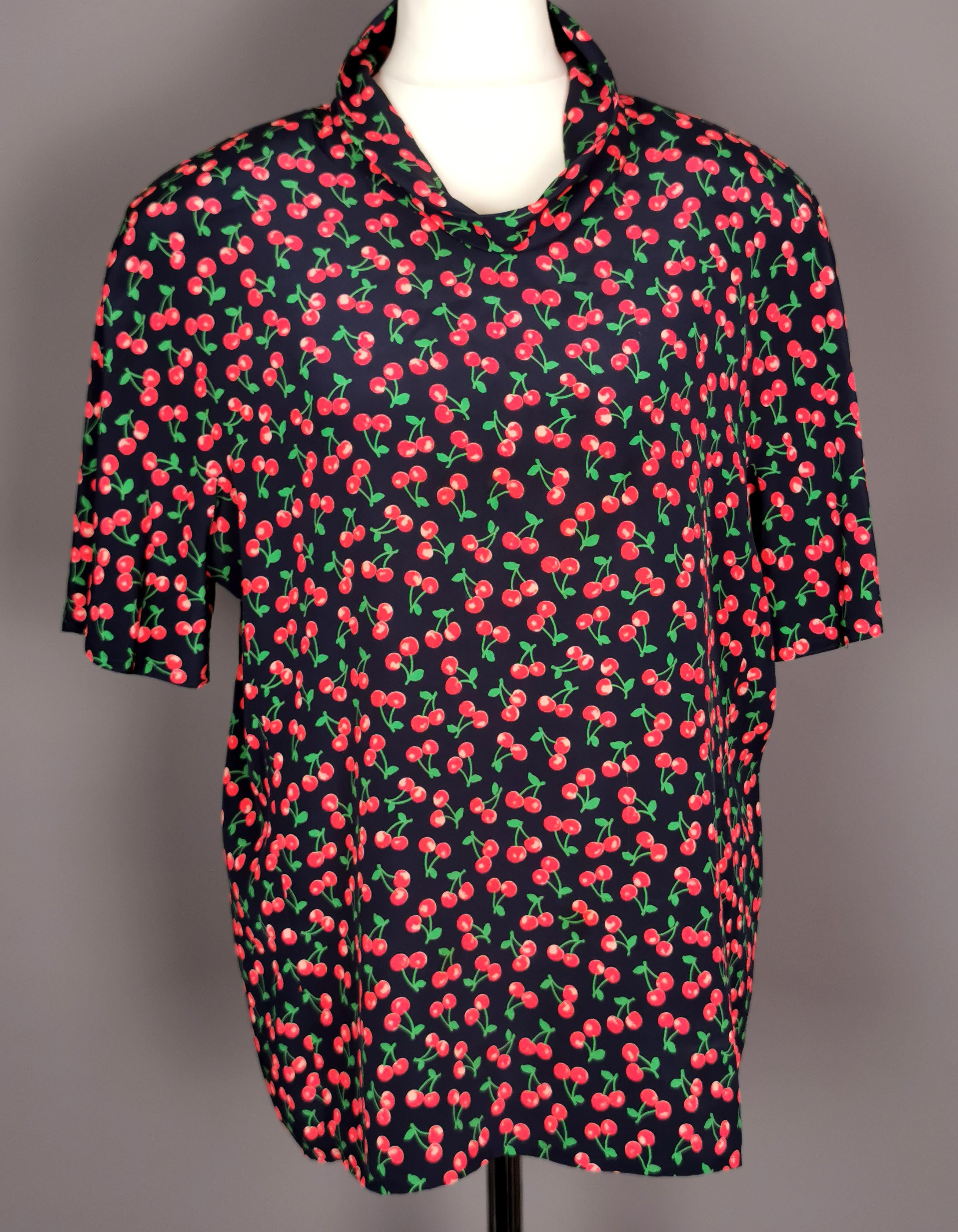 A gorgeous vintage c1980s Valentino Miss V cherry print Silk blouse.

It has a lovely all over cherry print on a soft dark blue silk ground.

The blouse has short sleeves and original shoulder pads.

It has a rolled neck and a concealed half zipper