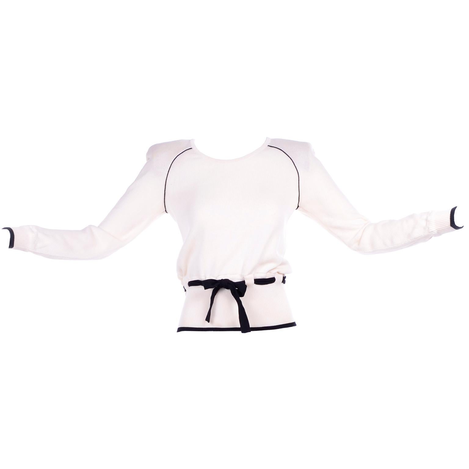 This is a lovely Valentino ivory, almost white cotton sweater with black trim along the hem, cuffs, and raglan sleeve seam, as well as a black waist tie. The waist tie goes through loops and is adjustable. It has sewn in shoulder pads that can be