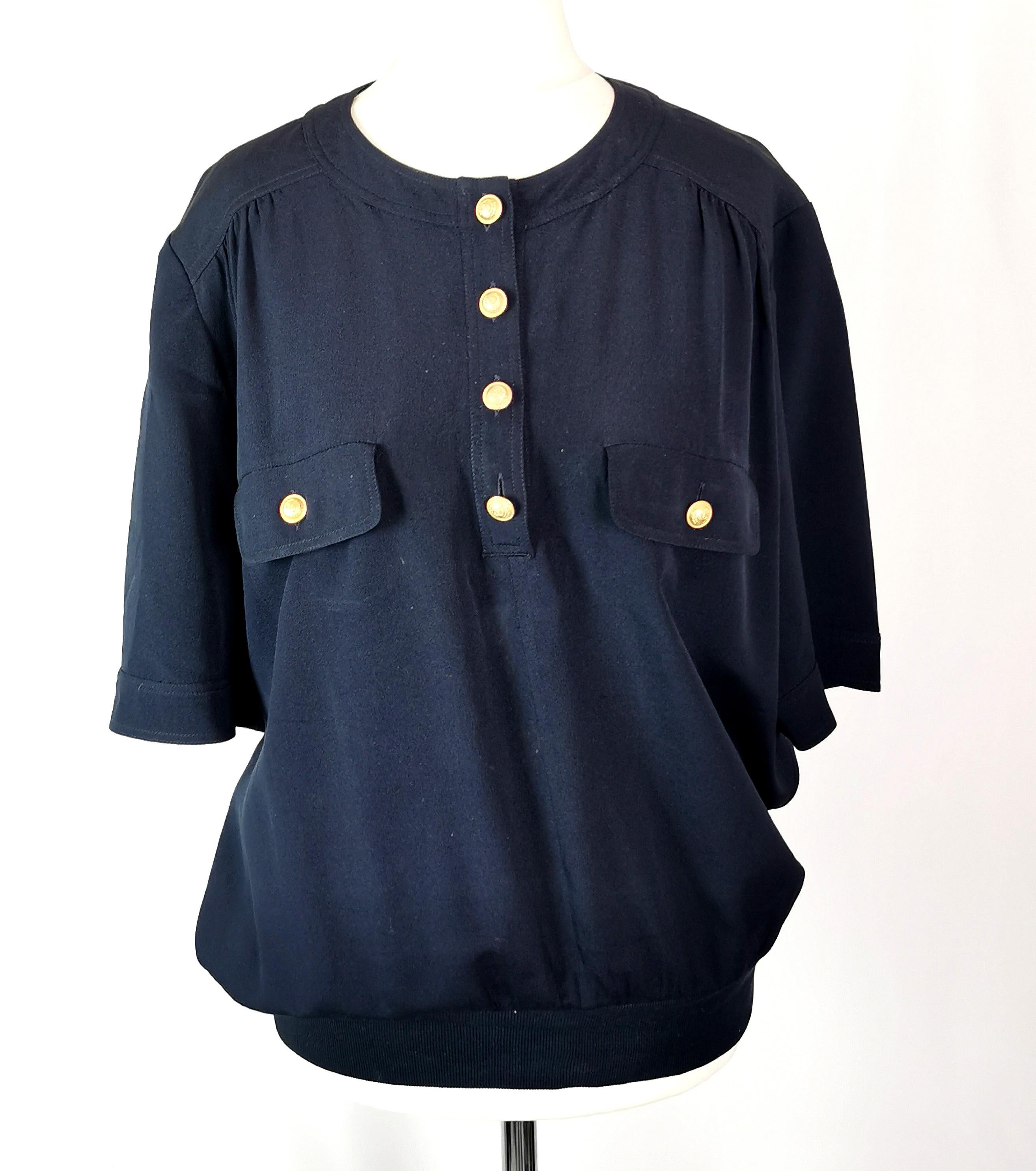A gorgeous vintage c1980s Valentino Miss V navy blue crepe Silk blouse.

It has a lovely nautical vibe to it in a pullover style with a knitted waistband and short sleeves.

It has buttons half the way up with gold tone monogrammed buttons.

It has