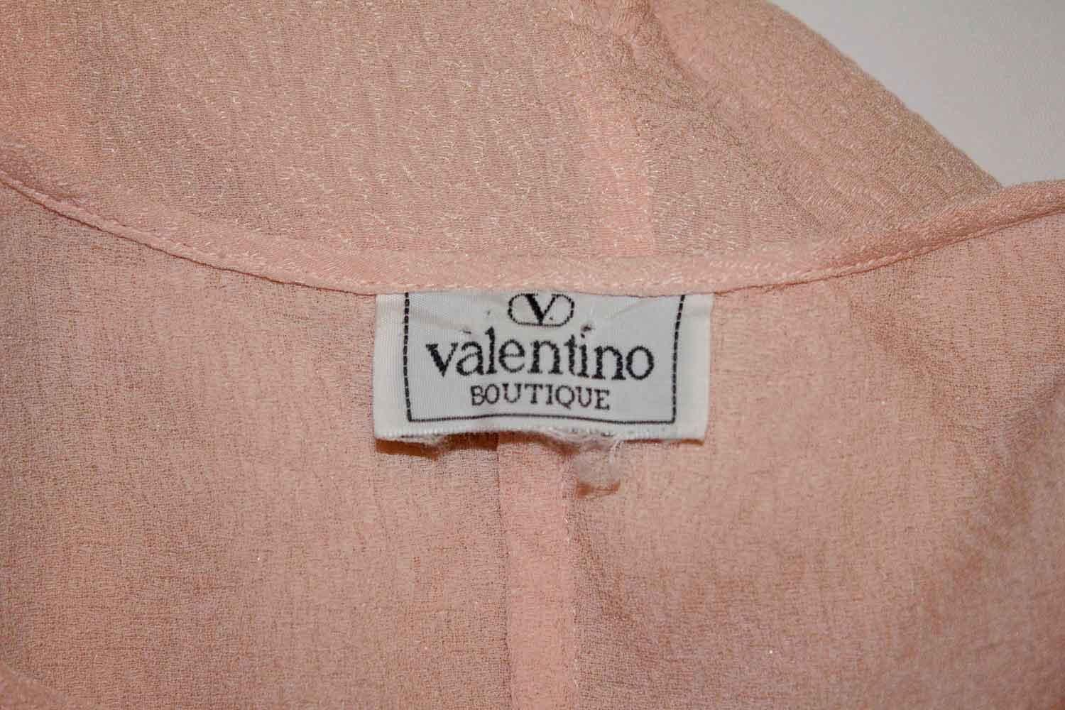 A pretty pink textured silk blouse by Valentino, Valentino Boutique. The blouse has a round neckline, with pleats on the front. The sleaves are tapered with zip openings. It has slits on the front, back , and either side of 11''. Made in Italy,