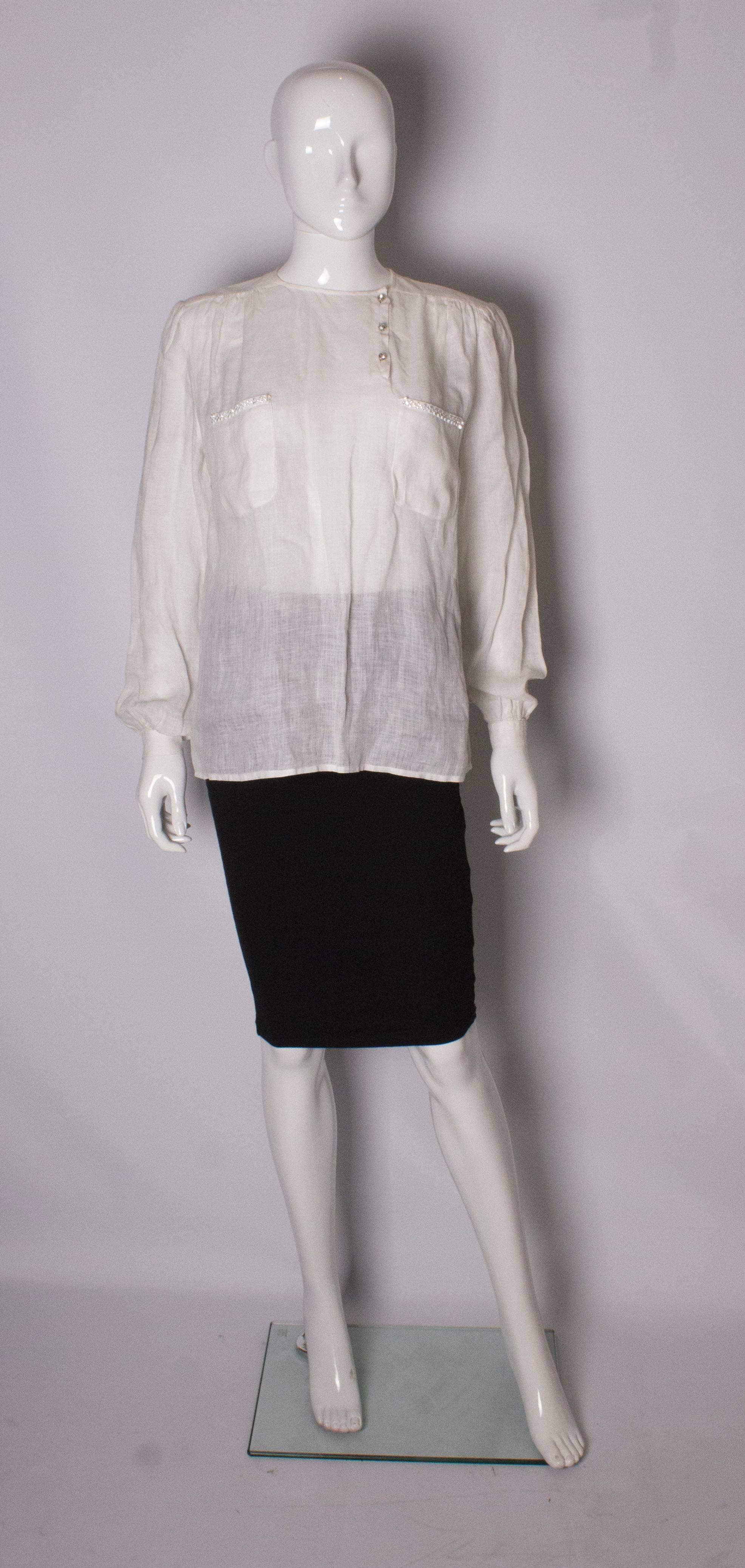 A white linen blouse by Valentino, Boutique line. The blouse has a round neckline, with off centre opening with three buttons. It has single button cuffs and 2 breast pockets with diamante decoration. It is worn loose and can fit bust up to 40''