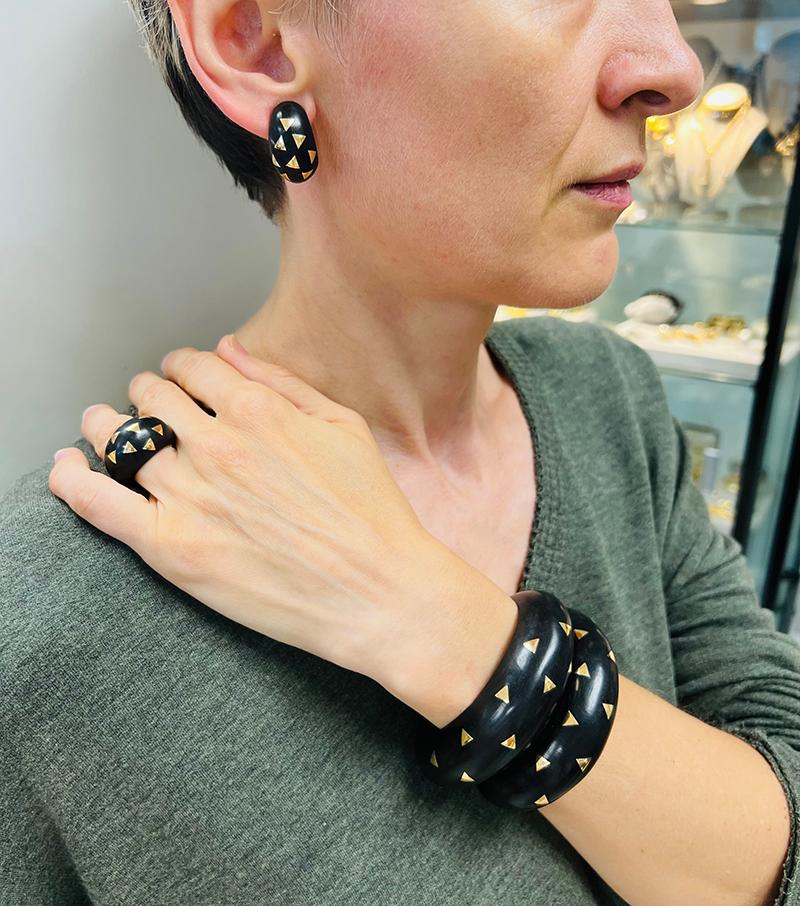 A stunning Van Cleef & Arpels set of two bracelets, earrings and a ring. The vintage suite is made of ebony wood with 18 karat yellow gold inlay.
All pieces have a similar spherical dome shape. The gold inlay is designed as the triangles lining up