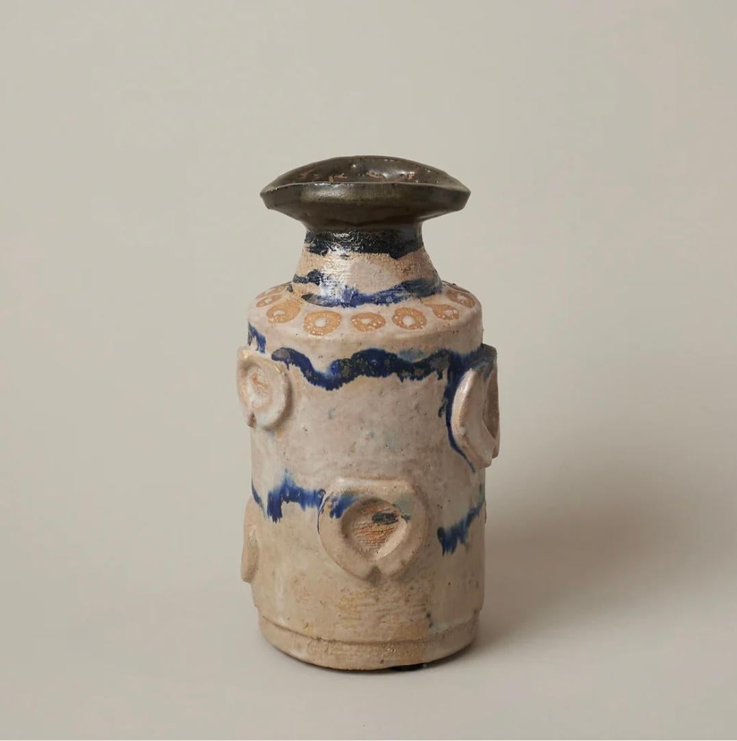 L'aspect rustique et artisanal de ce vase est conçu pour souligner son caractère unique. Les couleurs moutarde et bleu et les motifs de l'émaillage font passer la pièce du statut de poterie fonctionnelle à celui d'œuvre d'art en céramique.