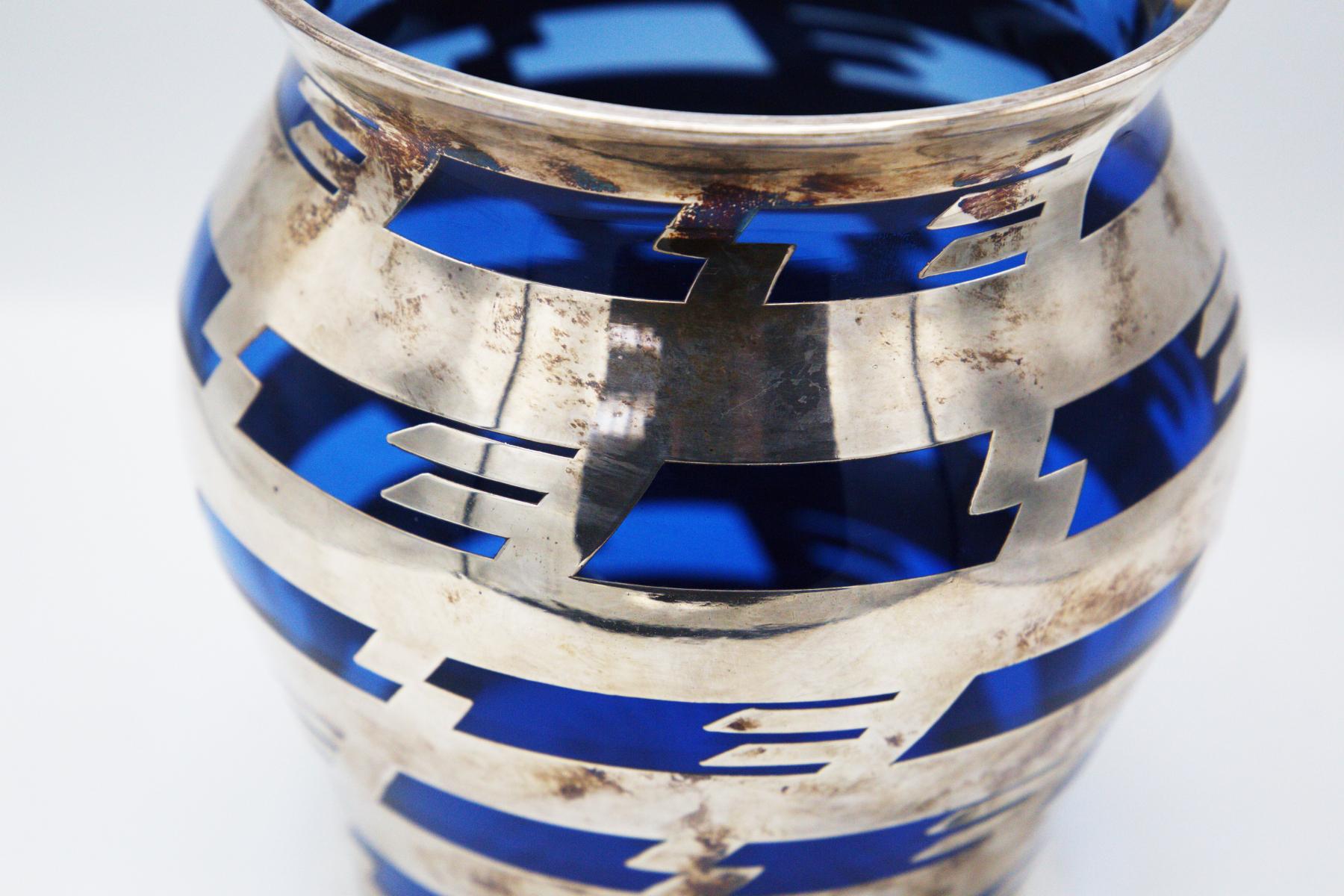 Magnifique vase en verre bleu vintage conçu par Bacarat dans les années 1920.
Le vase est fabriqué en métal argenté dans sa structure et, à travers un tissage à tissage à tissage plat, il crée un merveilleux effet d'entrelacement avec le verre