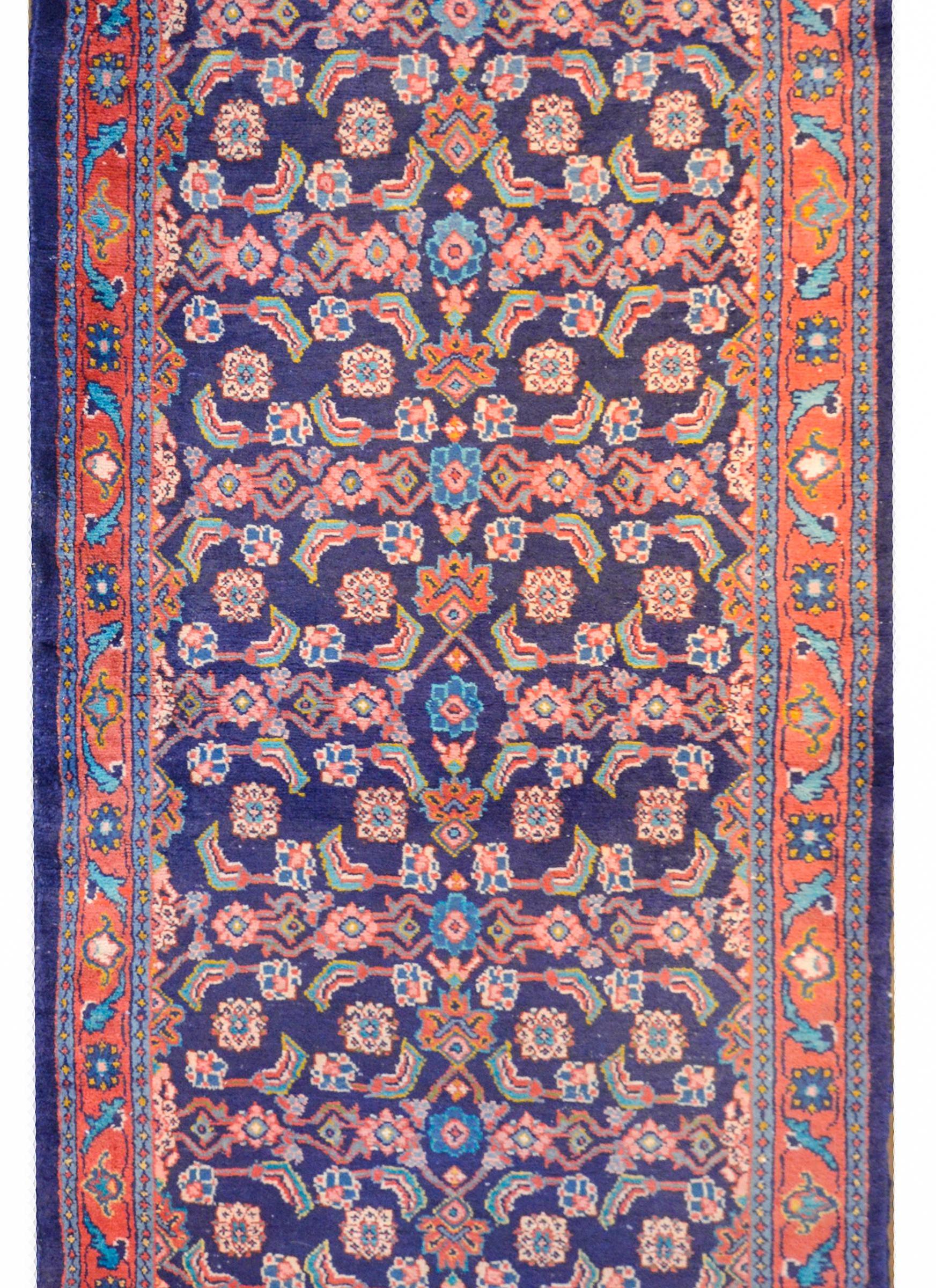 A wonderful vintage Persian Veese runner containing a traditional Herati pattern with an all-over trellis pattern of flowers and leaves woven in myriad colors on a dark indigo background surrounded by a large-scale floral and leaf patterned border.
