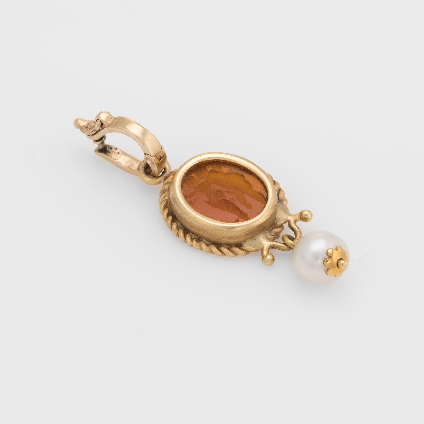 Finely detailed Venetian glass pendant, crafted in 14 karat yellow gold. 

Venetian glass in an amber hue measures 10mm x 8mm and features an intaglio of two winged cherubs. One 6mm cultured pearl is attached to the base of the pendant.

The pendant