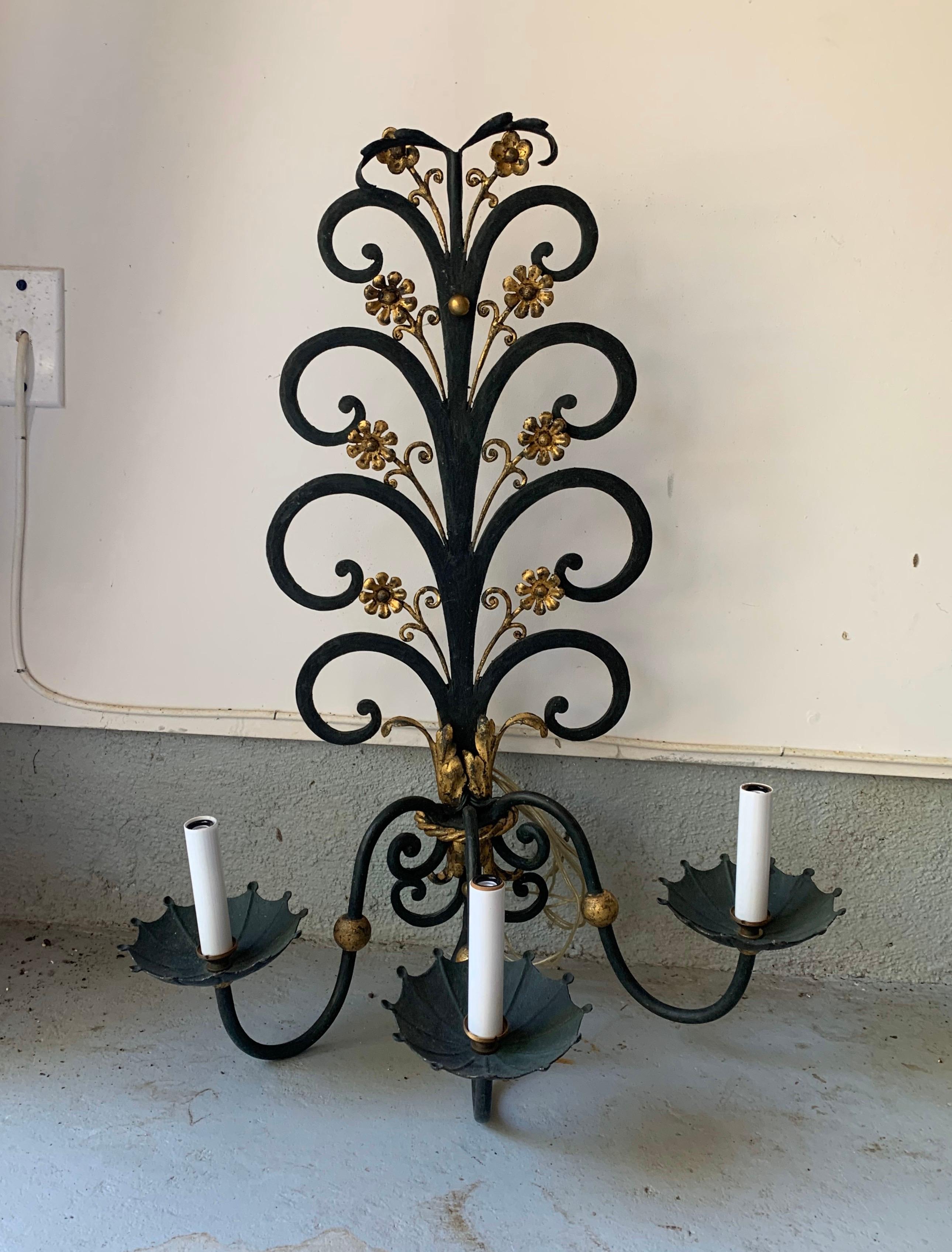 A pair of fanciful verdigris or dark green metal sconces accented with brass florettes and decorations, each having three arms and faux candlesticks, circa 1980.

Wired for USA; each sconce takes three chandelier base bulbs, 40 watts max each.