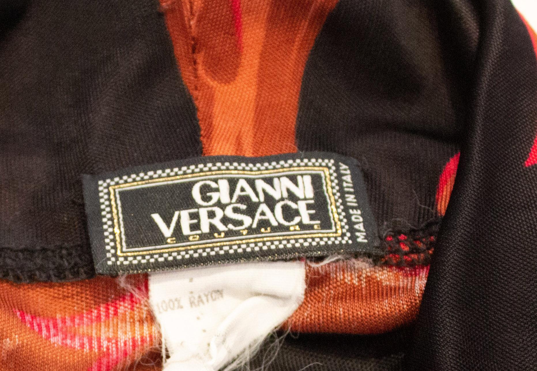 Un top chic de Versace Couture.. El top tiene cuello de capucha, fondo negro con un estampado rojo y marrón.  Se ajusta a un busto de hasta 42'', pero es mejor llevarlo suelto.