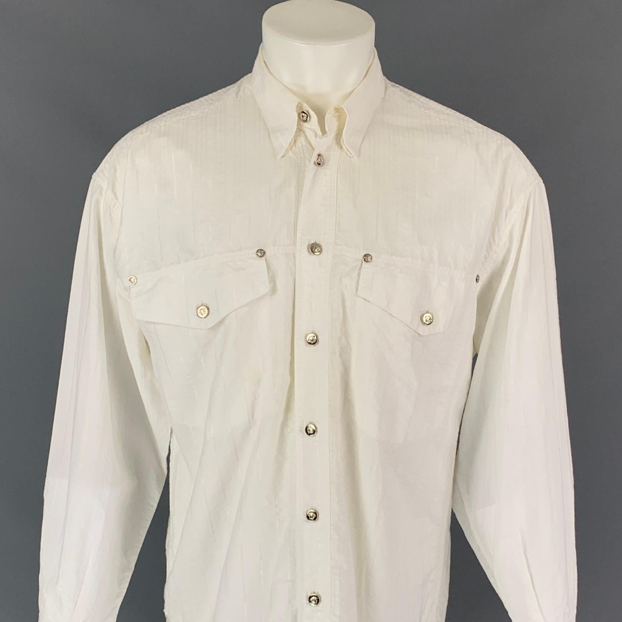 Vintage VERSACE JEANS COUTURE Langarmhemd aus weiß gestreifter Baumwolle mit folgenden Eigenschaften: Vordertaschen, gespreizter Kragen, silberfarbener Medusa-Knopfverschluss. Hergestellt in Italien. 

Guter gebrauchter Zustand. Kleiner Fleck auf