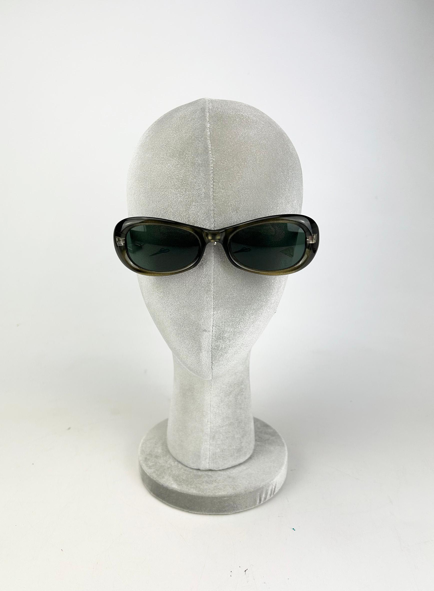 Vintage Versace Olive Green Oval Frame Sunglasses c1990s in good condition. Olive green frame with slight cat eye sheen throughout trimmed with silver hardware and dark gray oval cut lenses. Signature Versace medusa along both front end of each arm.