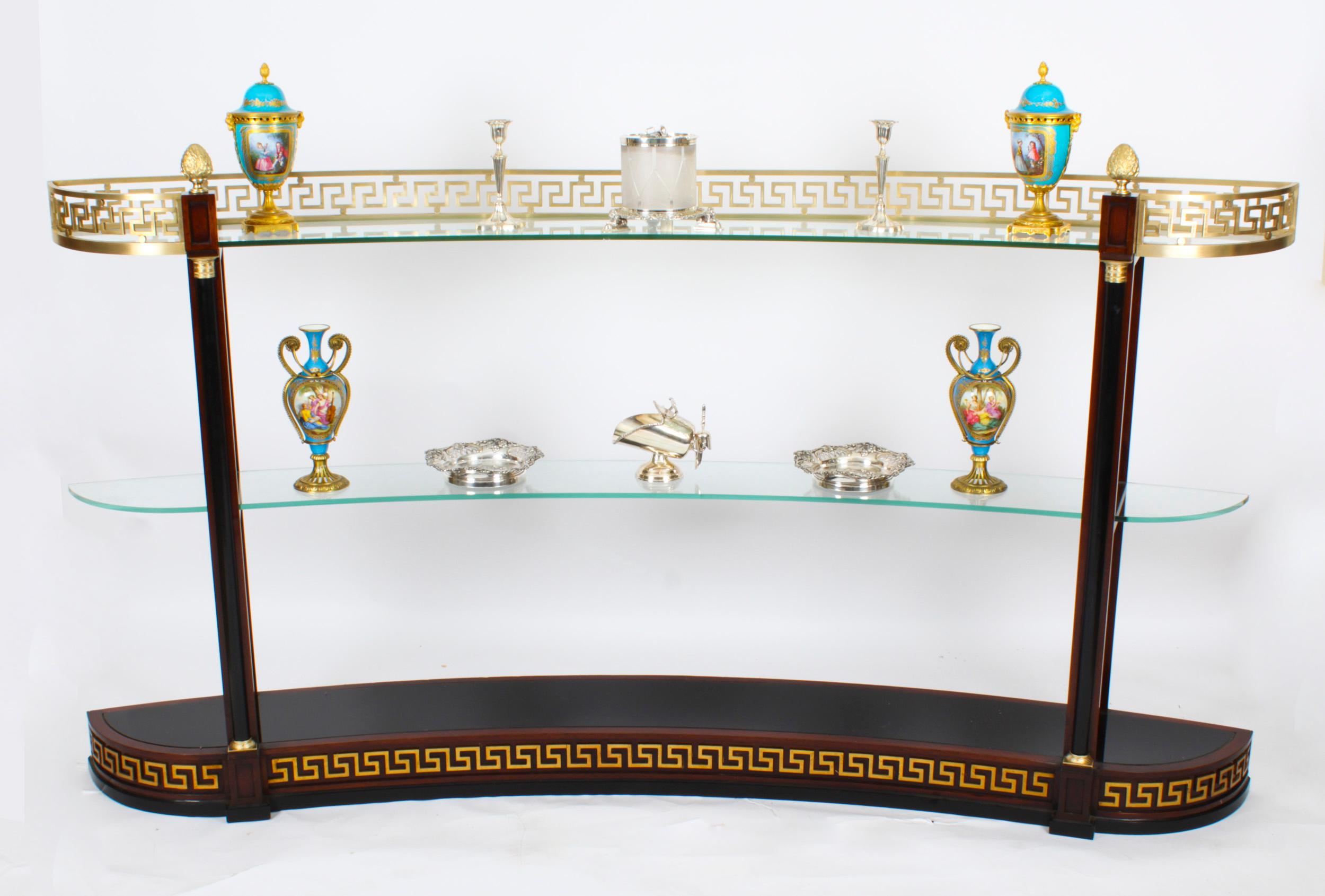 This is a magnificent vintage walnut and ormolu mounted Versace curved glass display unit, circa 1990's in date. 

This free-standing unit features a Greek key ormolu gallery over two open shaped glass shelves, the walnut frame with black lacquer
