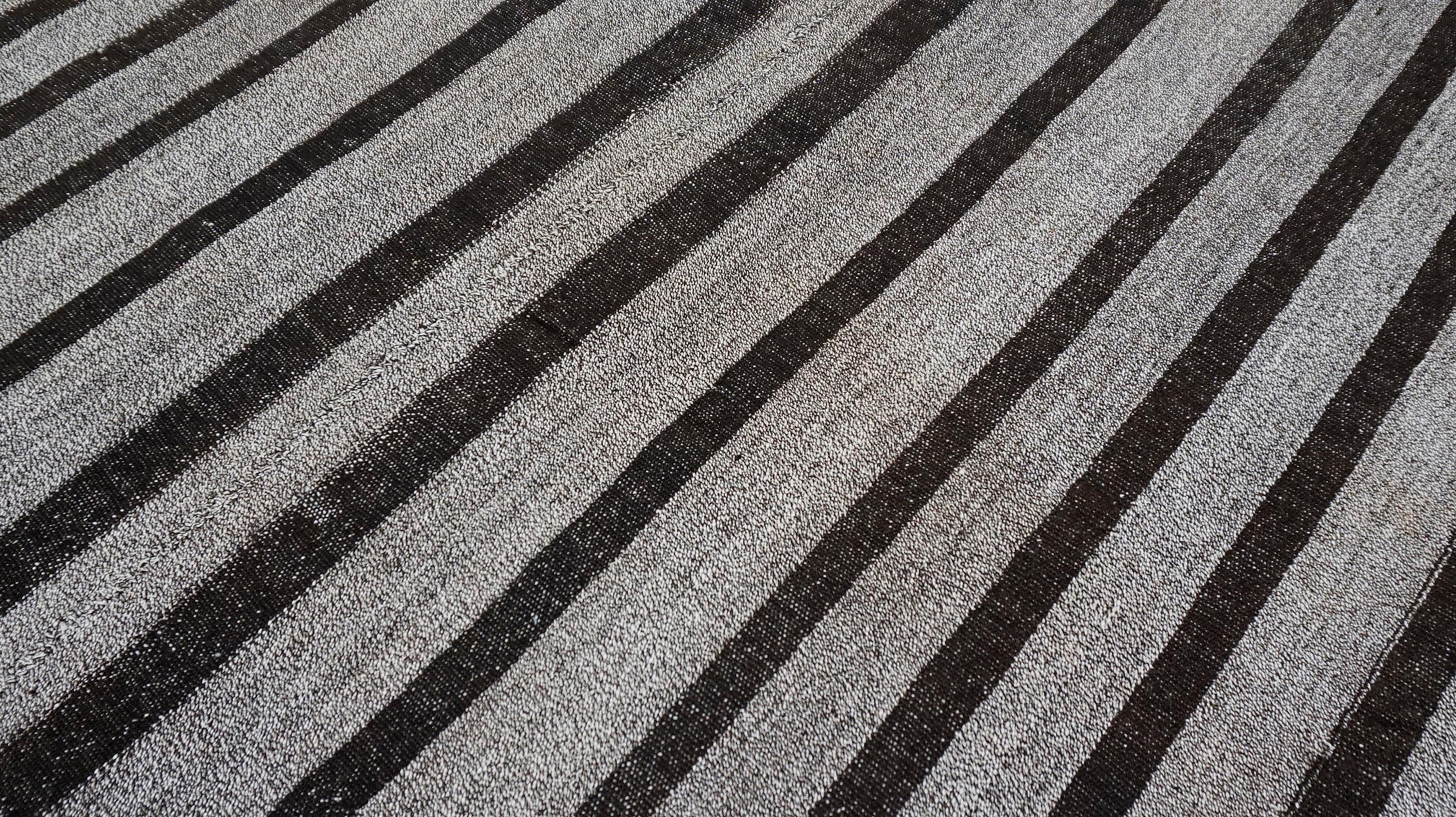 Dieser auffällige, flachgewebte Vintage-Teppich zeigt ein zeitloses, minimalistisches Design, das aus einer Mischung aus handgewebter Wolle und natürlichen Hanffasern hergestellt wird. Das Stück ist mit einem rhythmischen vertikalen Streifenmuster