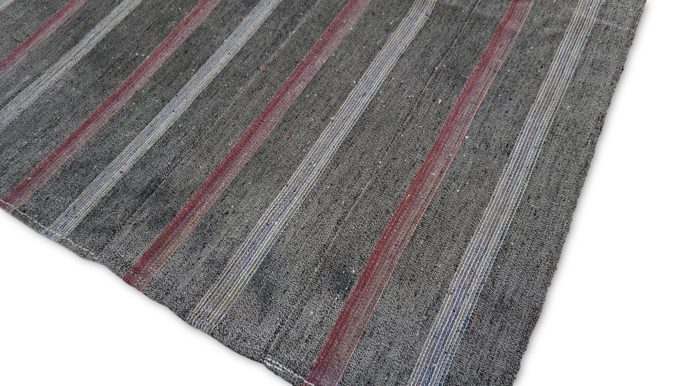 Ce tapis vintage en laine kilim présente un motif intemporel de rayures verticales dans des tons anthracite, gris et des accents roses subtils, créant un équilibre élégant entre les esthétiques rustique et moderne. La palette de couleurs sourdes et