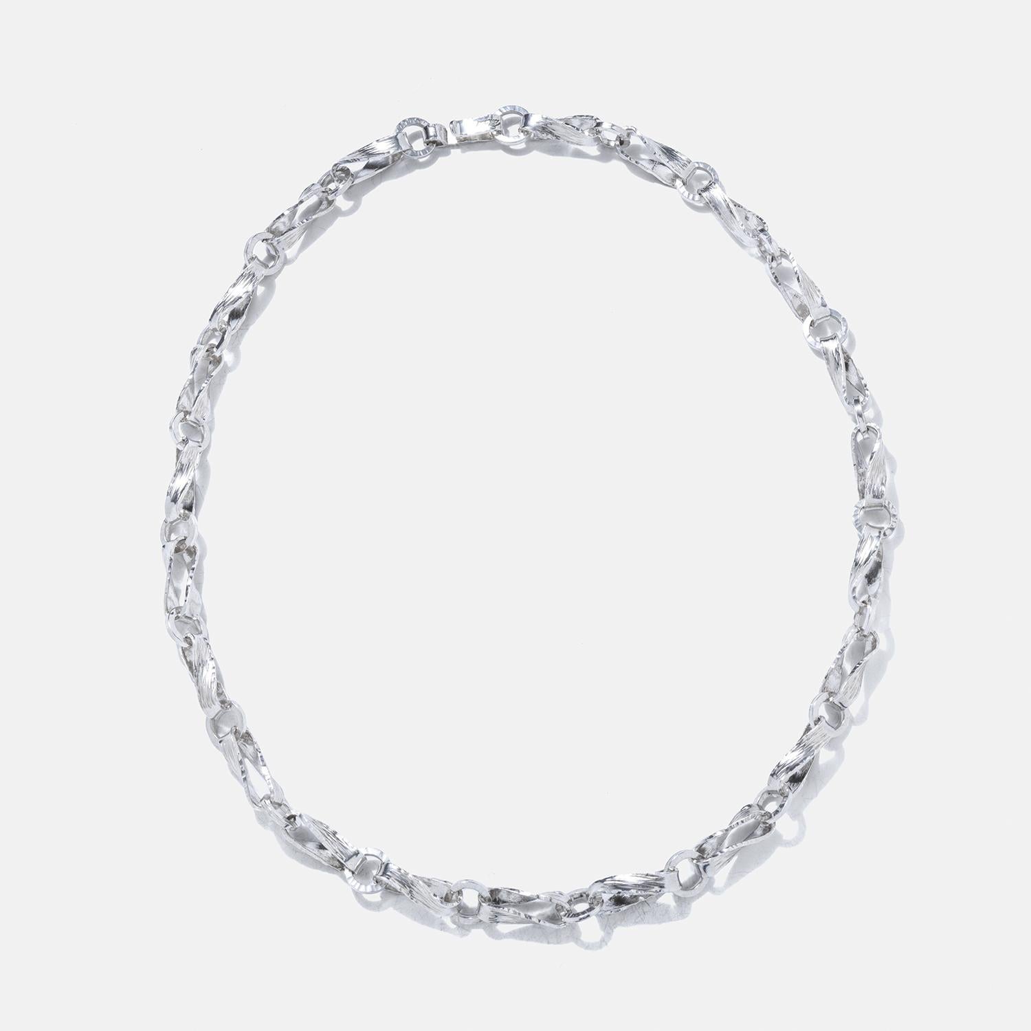 This substantial sterling silver necklace features a playful ring and bar chain design, with links that are artfully twisted to create a dynamic and eye-catching appearance. The surface of the necklace is finished with a texture, giving it a