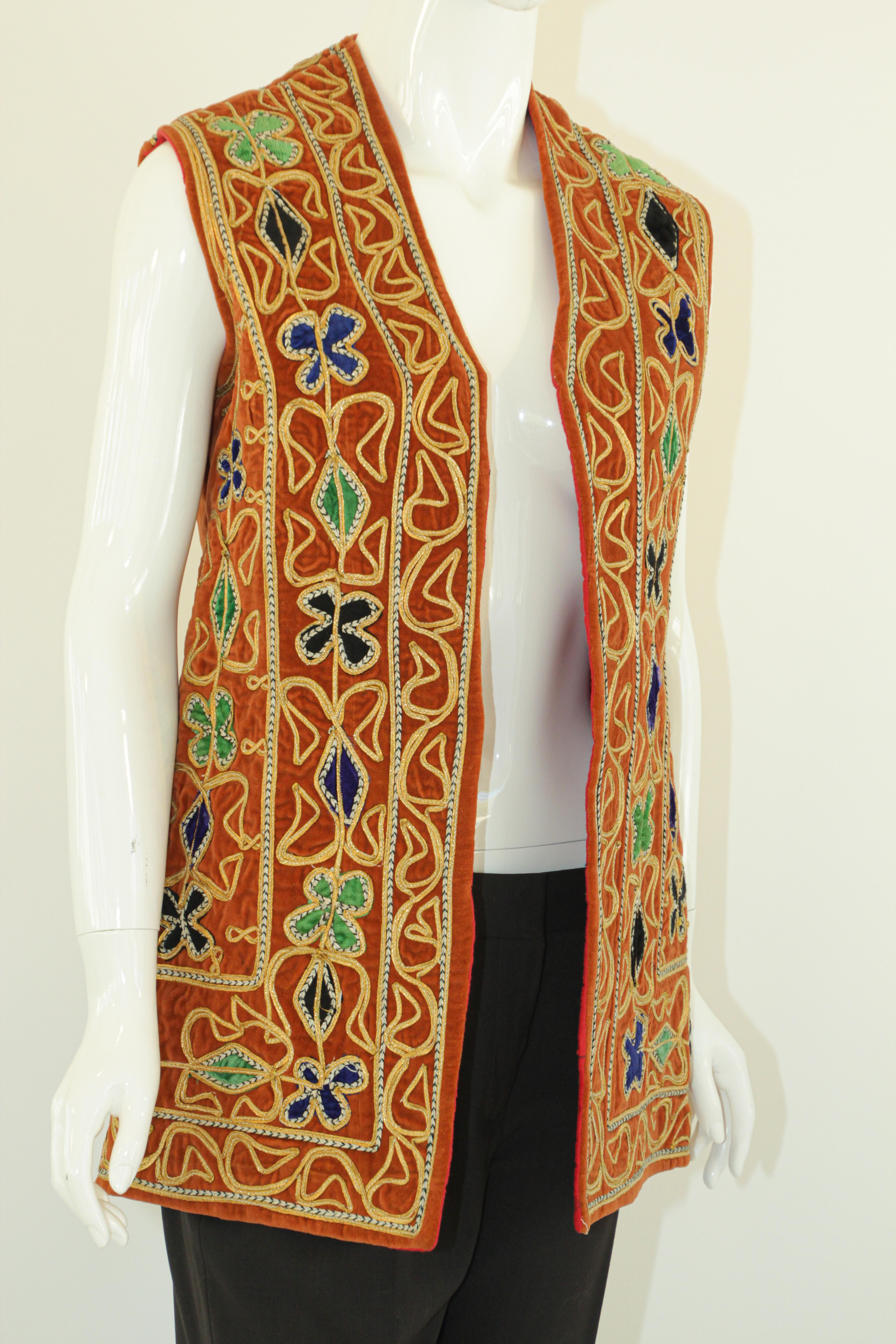 Vintage ethnic vest brightly colored embroidered design of geometric patterns in blue, yellow, green, gold, against a burnt orange brown velvet ground, lined in red.
Asian, Middle Eastern, Turkish or Afghanistan ethnic folk costume.
Great colorful