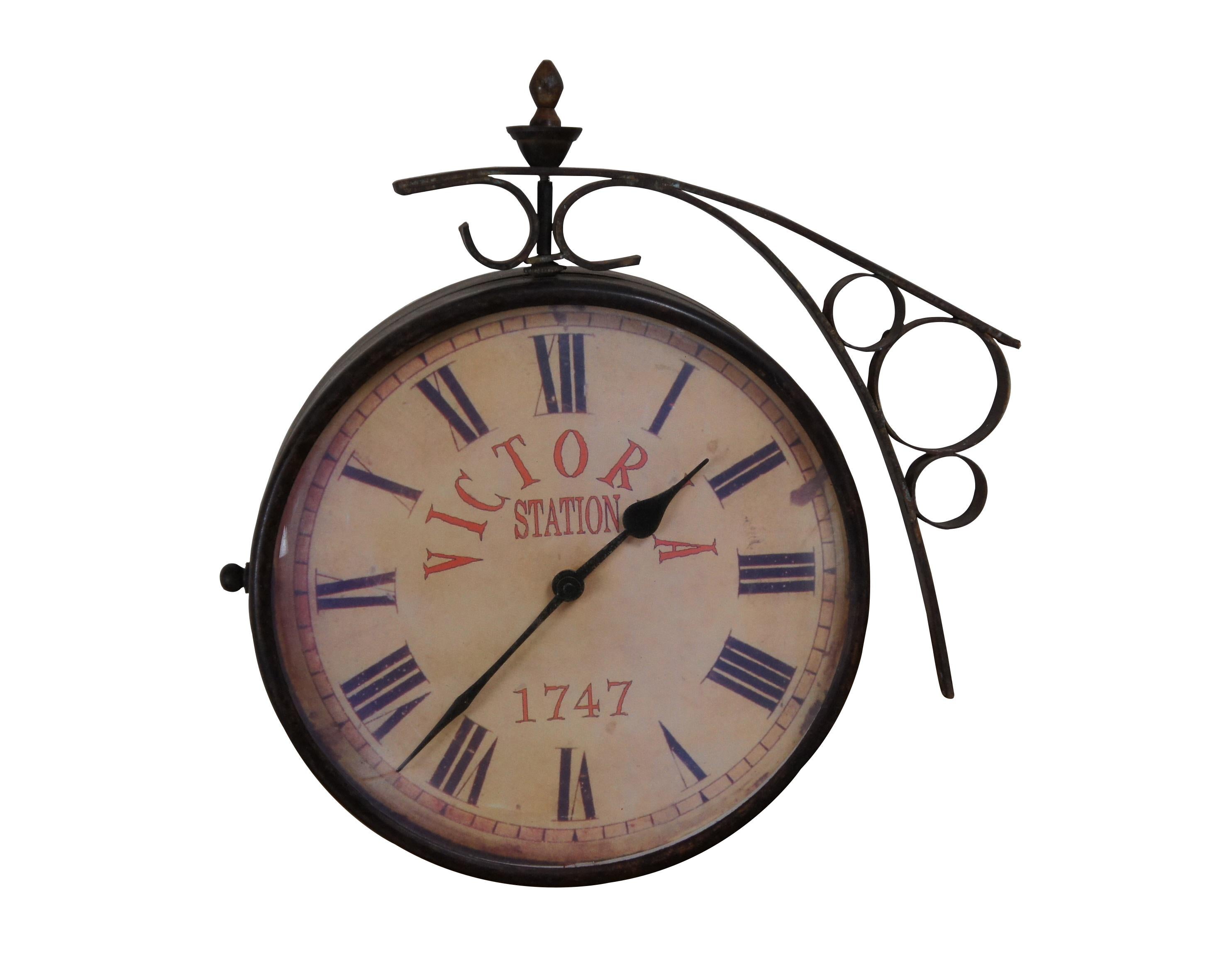 Late 20th century double sided railway clock styled after the famous clock at Victoria Station, London. Wrought metal wall mounted support and case in a dark bronze finish. 10 inch diameter printed face with faux distressing, Roman numerals, and the