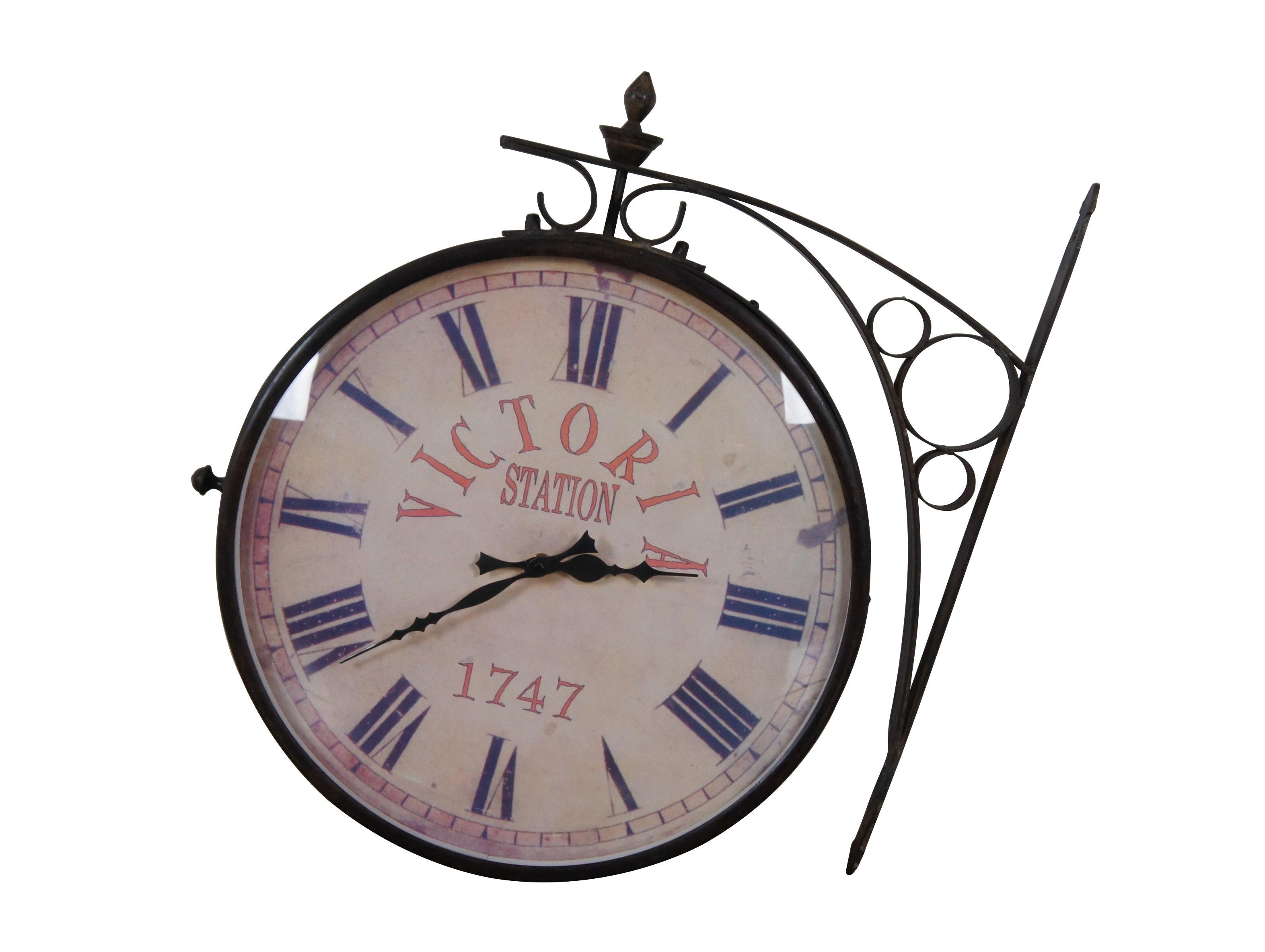 2 Available - Late 20th century double sided railway clock styled after the famous clock at Victoria Station, London. Wrought metal wall mounted support and case in a dark bronze finish. 14 inch diameter printed face with faux distressing, Roman