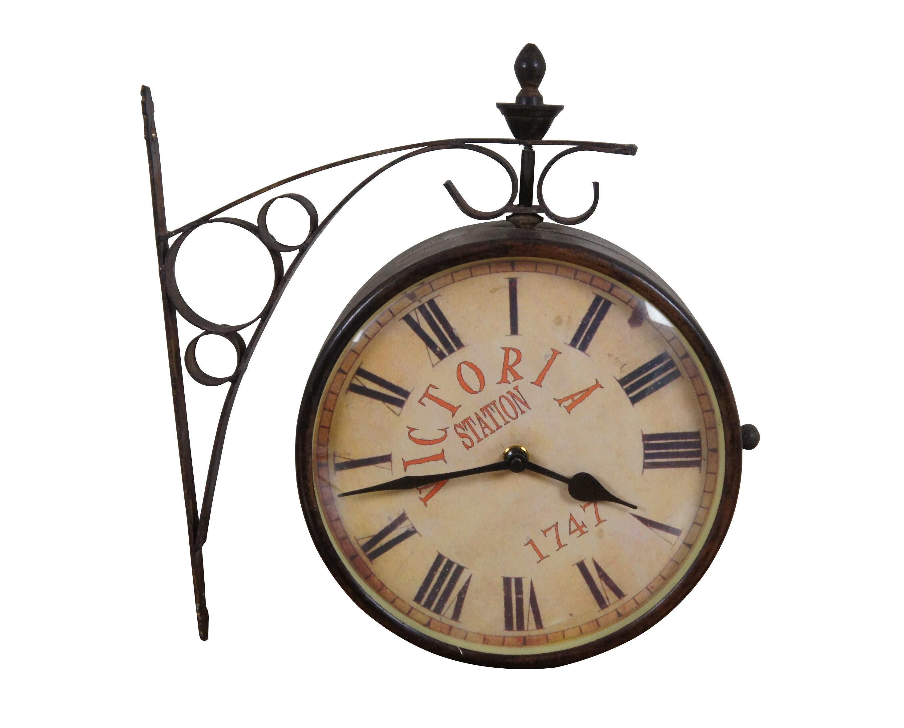 Late 20th century double sided railway clock styled after the famous clock at Victoria Station, London. Wrought metal wall mounted support and case in a dark bronze finish. 8 inch diameter printed face with faux distressing, Roman numerals, and the