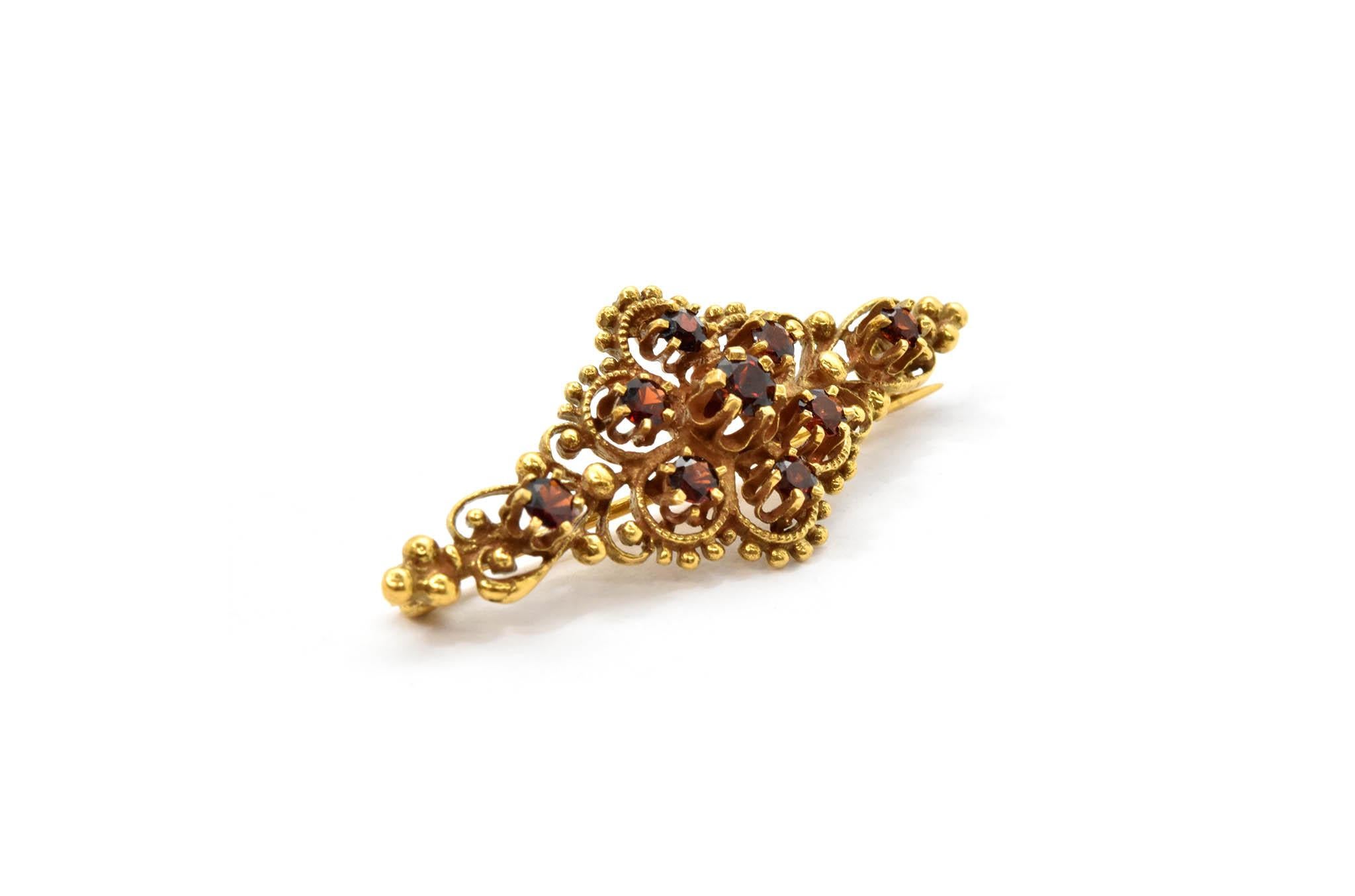 This 14k yellow gold pin features 9 round prong set garnet stones. The garnet stones have a total weight of 0.36ct. The pin measures 38x16mm and it weighs 3.97 grams.