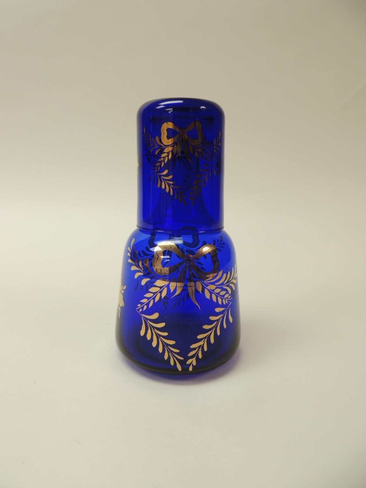 Vintage Victorian cobalt blue bedside table water decanter
Hand painted water decanter with tumbler water cup. Gold leaf bows, vines and flowers are in the motif of this hand blown bedside table water decanter.
Size: 4” D x 7.5” H.
 