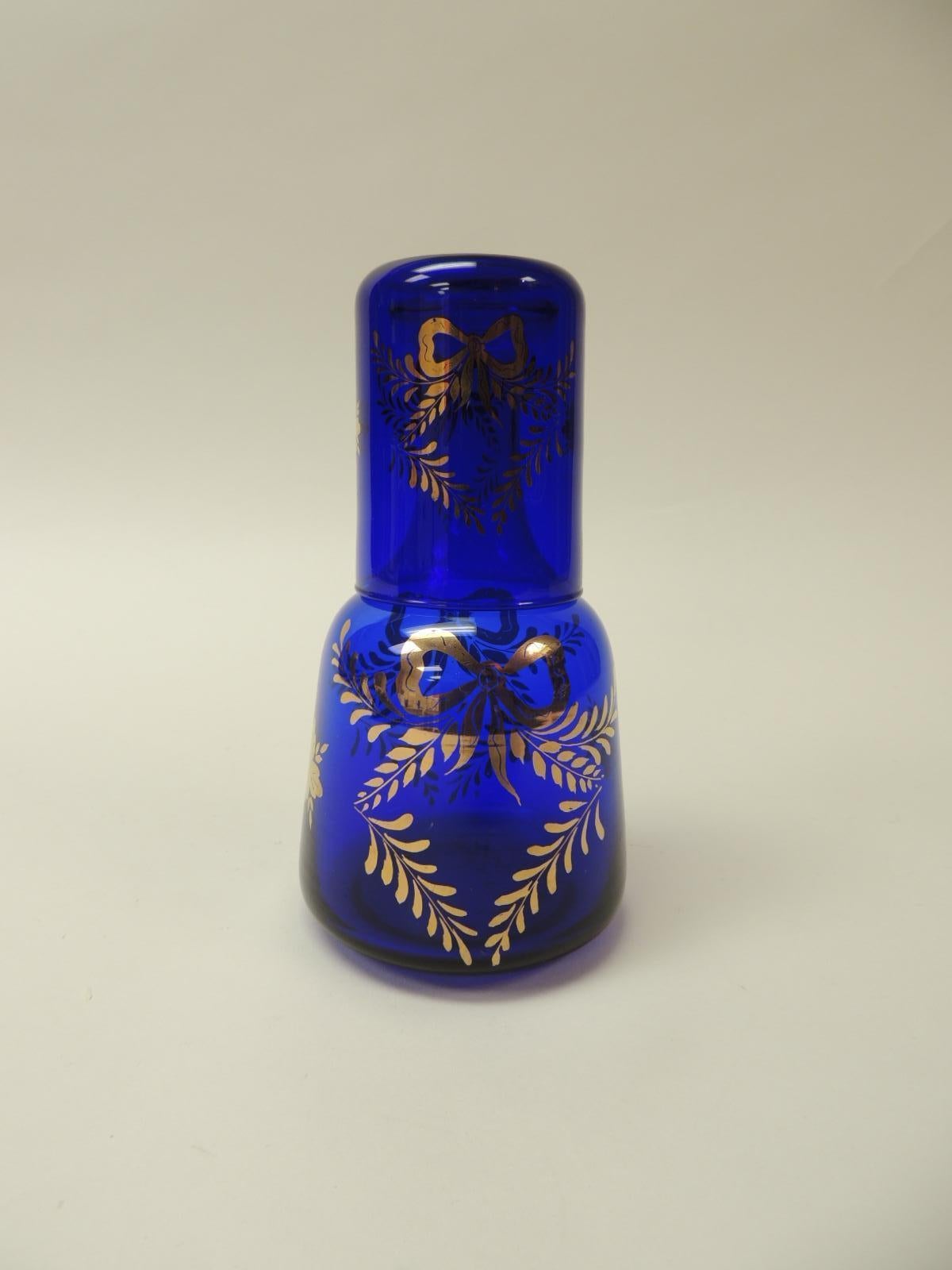 Vieille carafe de table de nuit victorienne bleu cobalt
Carafe à eau peinte à la main avec gobelet à eau. Des arcs en feuille d'or:: des vignes et des fleurs sont le motif de cette carafe de table de chevet soufflée à la main. 
Taille : 4