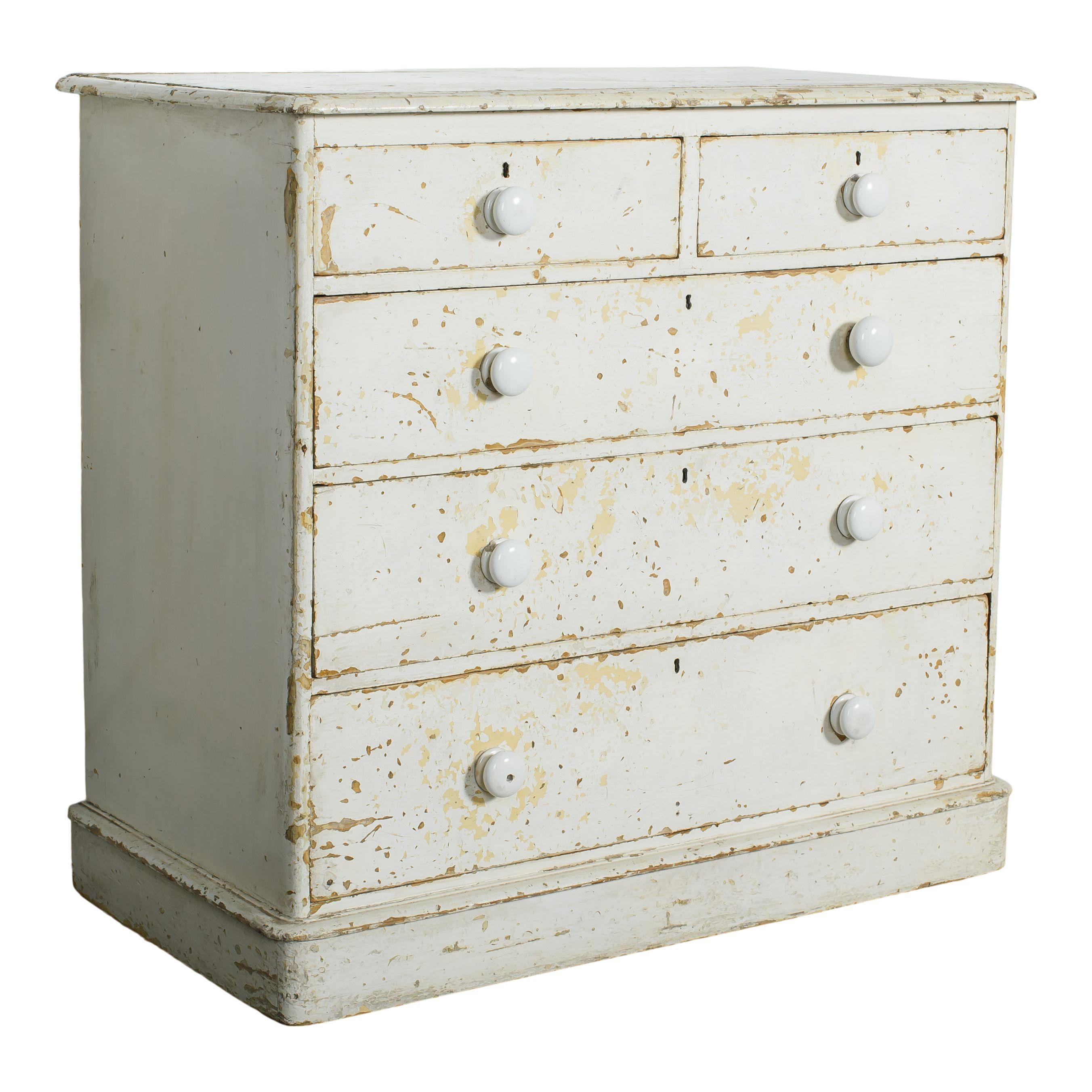 A beautiful antique wood dresser with worn white paint. This dresser has a simple design, with three wide drawers and two small ones. The original white paint is chipping and worn, giving the piece a vintage charm and history. The original ceramic