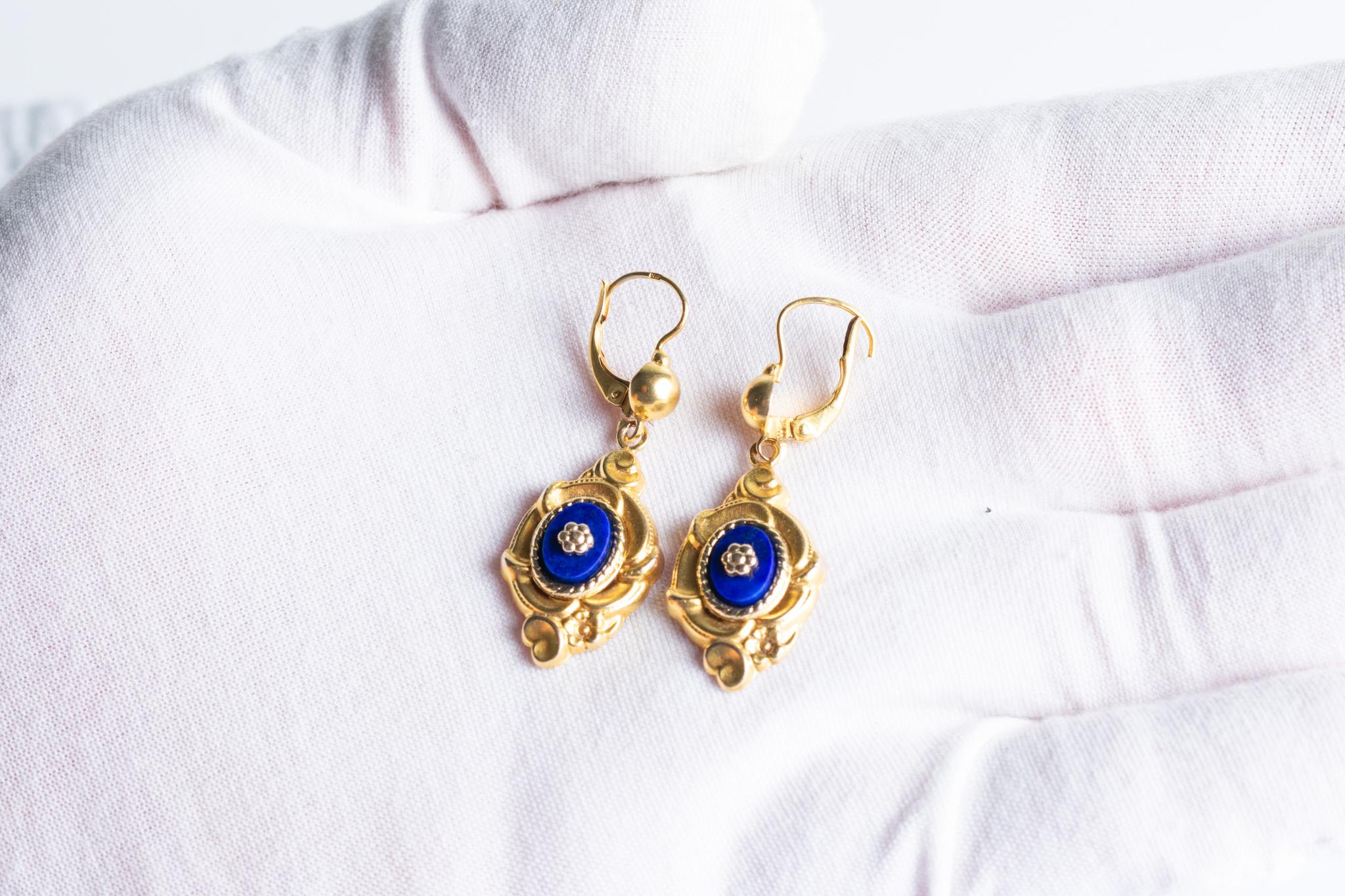 Un bellissimo ed elegante paio di orecchini vintage in oro giallo 14K in stile Victorian Revival decorati con vibranti cabochon di lapislazzuli blu cobalto con un motivo floreale al centro. Anche le cornici dorate sono riccamente decorate con un