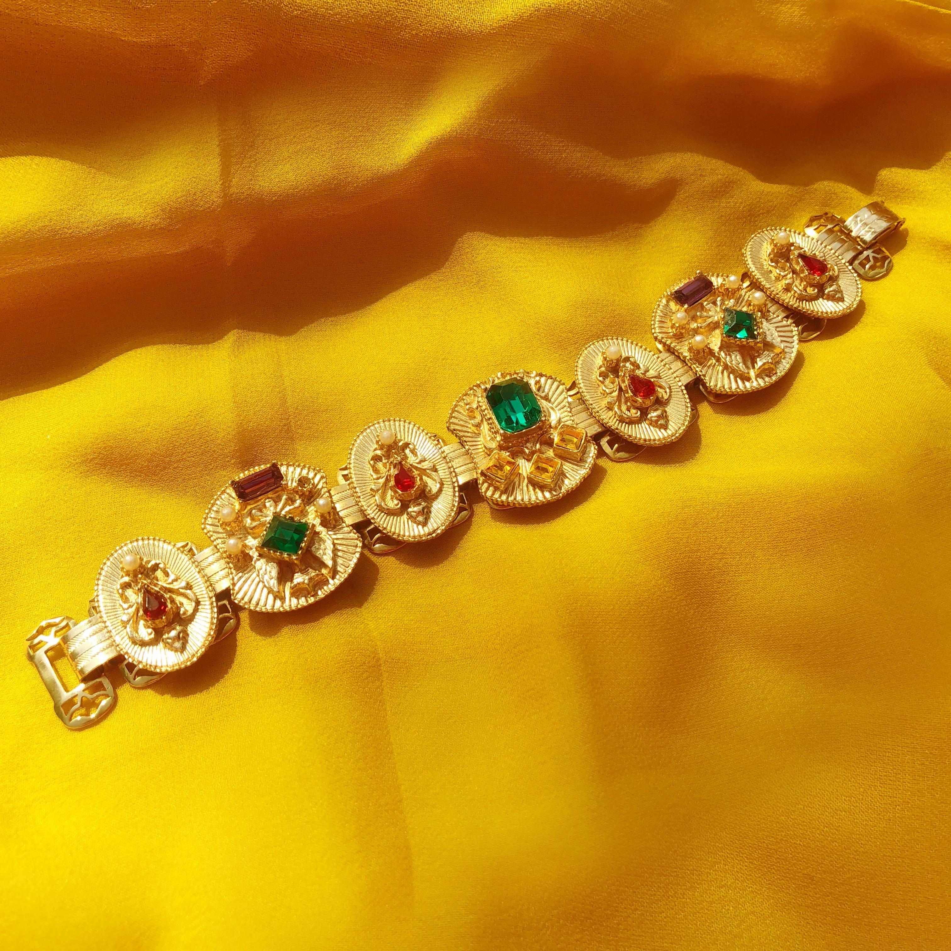 An absolutely gorgeous vintage gilded bookchain bracelet, circa 1960s; featuring seven gold-plated, rhinestone jeweled panels. Accented with tiny pearls and faceted crystal rhinestones in Emerald, Ruby, Amethyst and Topaz colors. An ornate piece to