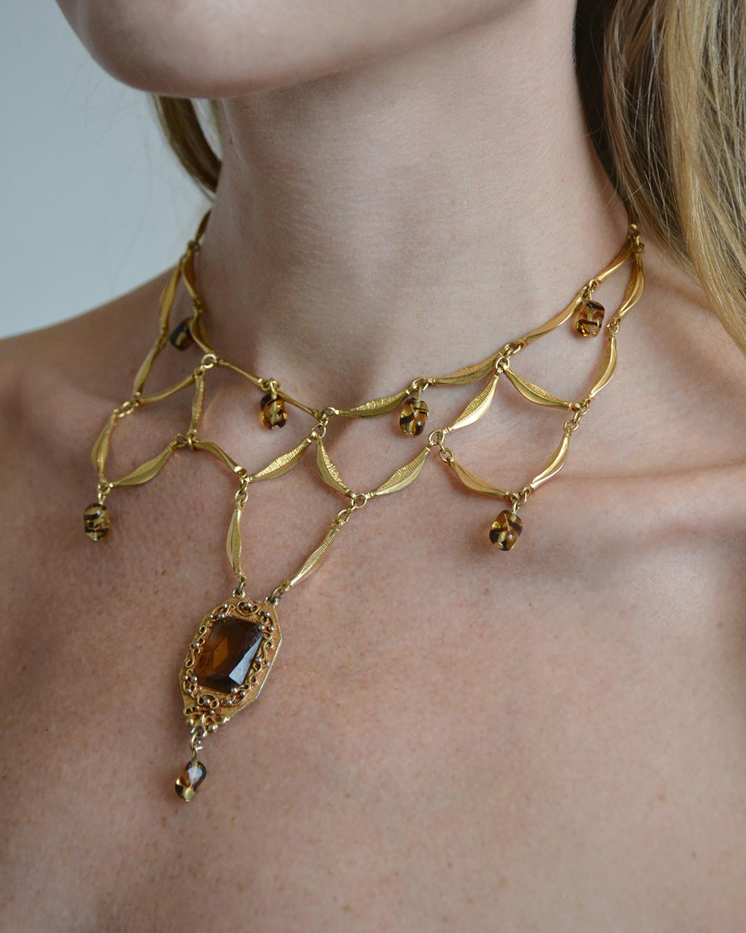 This incredibly elaborate vintage festoon necklaces is done in the style of the iconic Victorian festoon chokers of the late 19th century. It's features a lattice of gold, with a large topaz paste drop in an ornate setting, as well as smaller