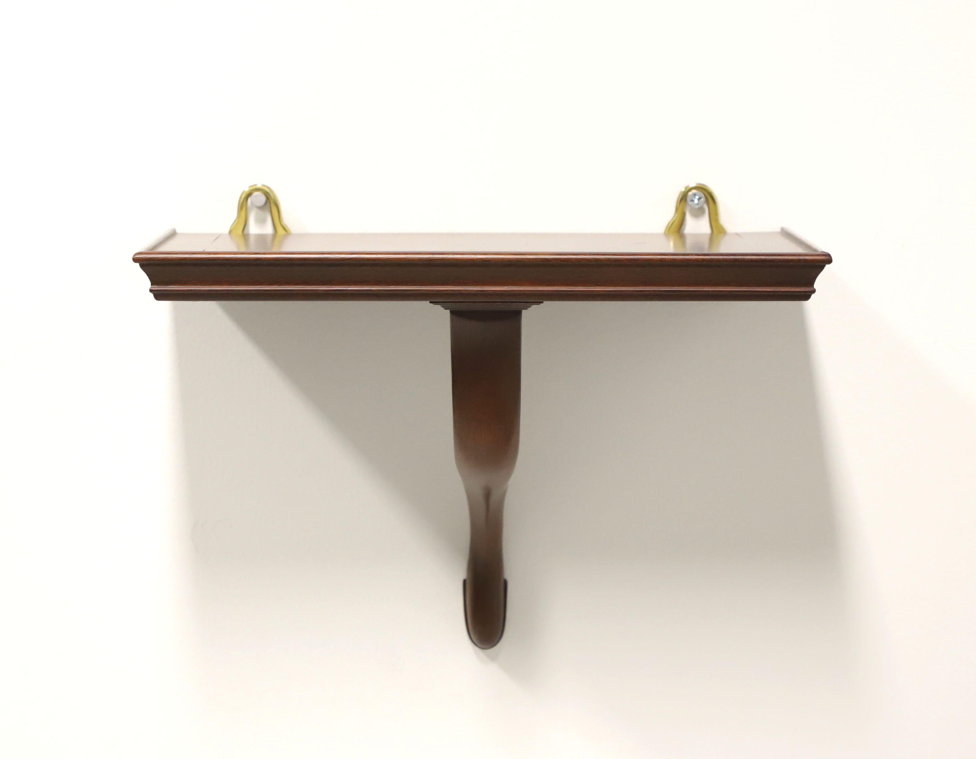 A Chippendale style petite wall shelf by Virginia Metalcrafters, from their Colonial Williamsburg Reproductions made exclusively for Colonial Williamsburg. Solid mahogany with flat display surface, dual brass hangers and curved leg support. Made in
