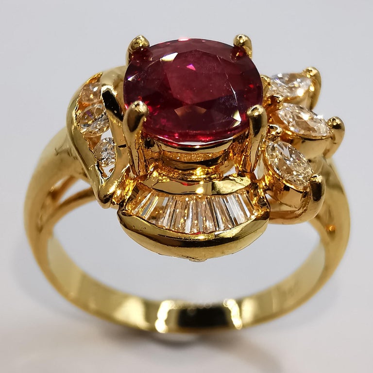 This vintage cocktail ring is a stunning piece of jewelry featuring a vivid red oval-cut ruby at its center, surrounded by a halo of sparkling marquise, tapered baguette, and round diamonds. The ruby is a vibrant and rich red color, adding a pop of