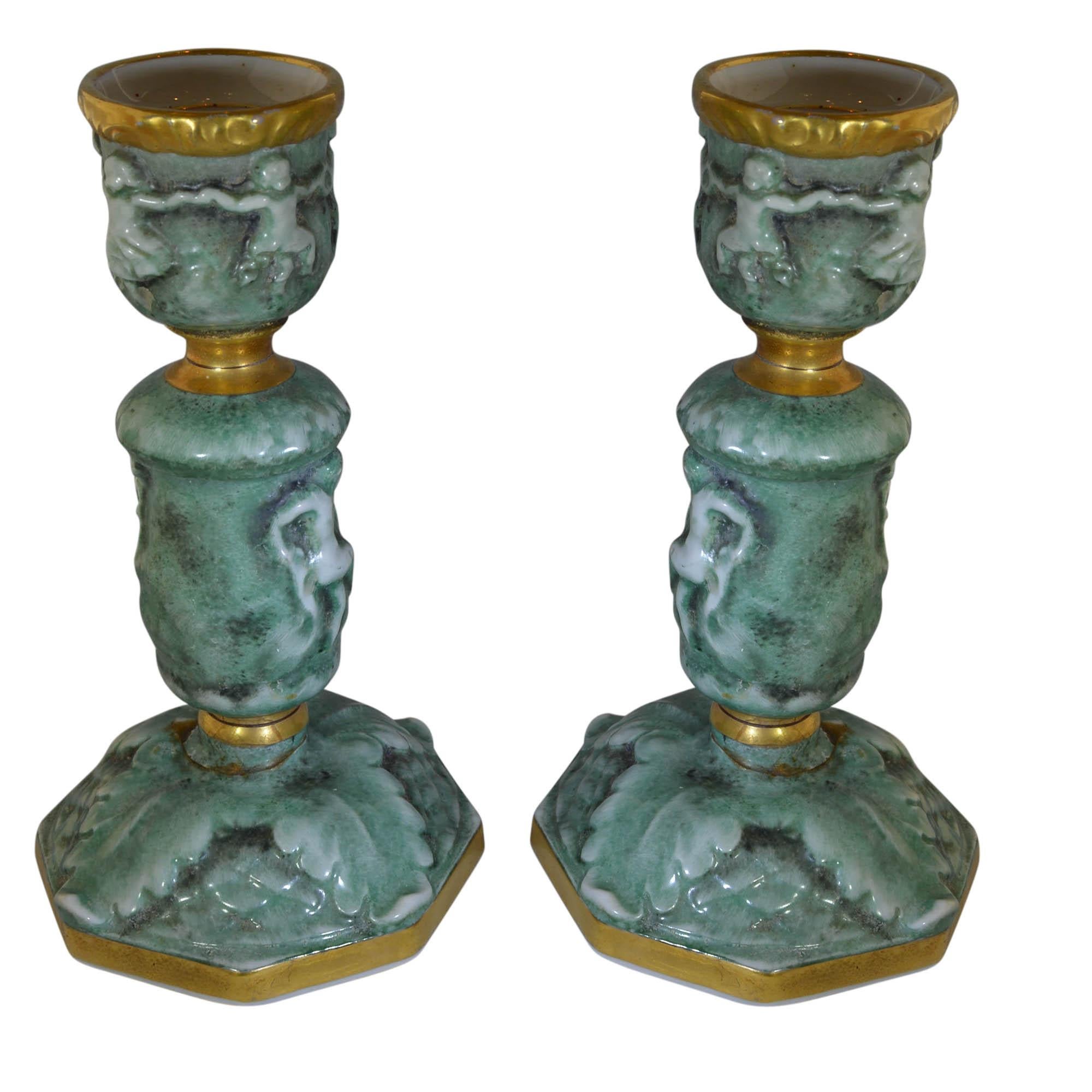 Vintage Von Schierholz candlesticks have putti dancing around the stems and feature a leaf pattern at the base. These heavily three dimensional detailed candlesticks are green with nearly white relief decoration. Gold gilt details. Makers mark.