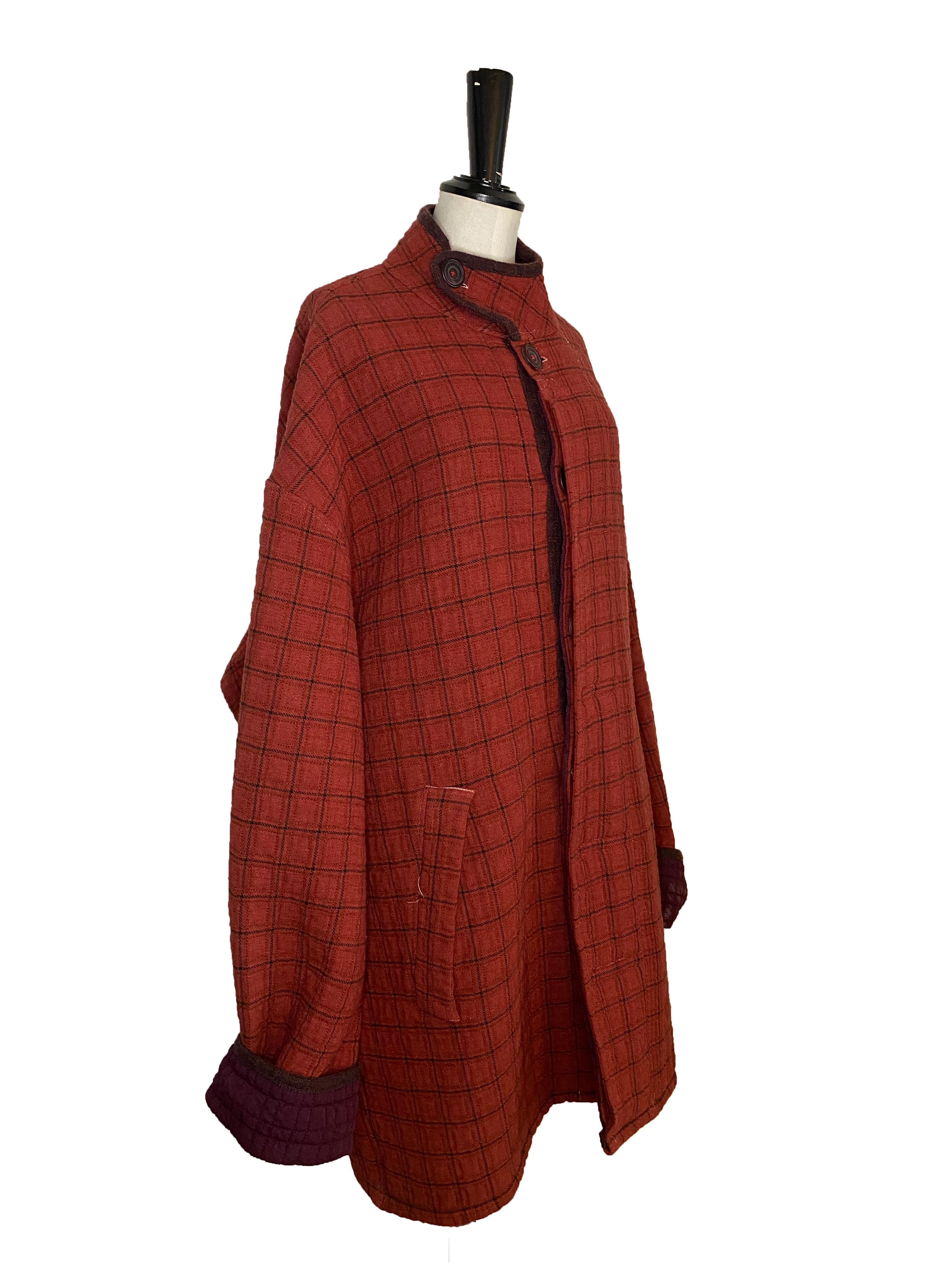 Manteau à carreaux pour hommes de Voyage Invest In The Original. Tige rouge rouille avec quadrillage et doublure violet foncé. Tissu double face. Bordé d'une tresse signée Voyage. Encolure asymétrique en forme d'entonnoir et poches profondes à rabat