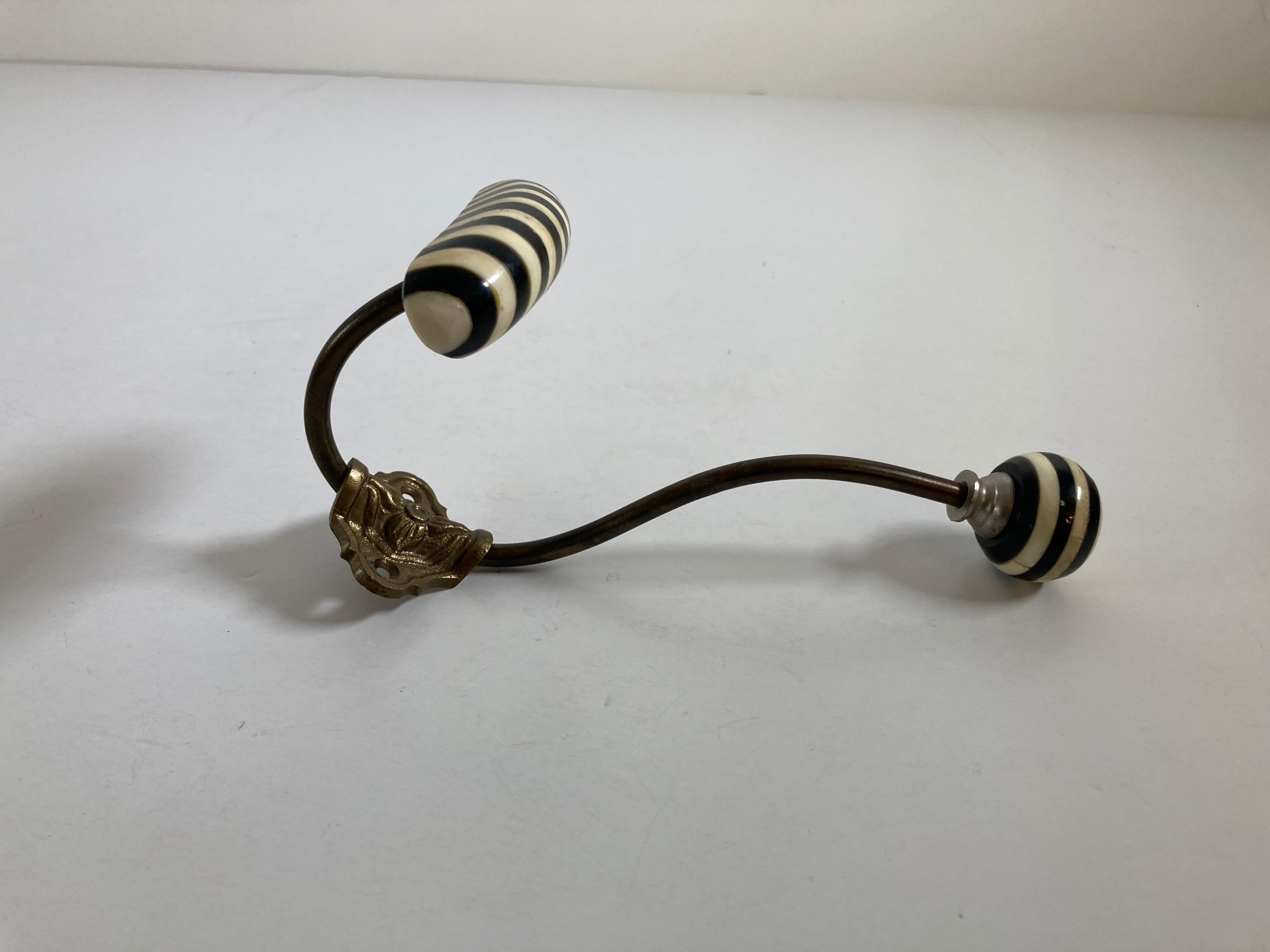 This is a vintage metal coat double hook with horn finals in black and white.
 This has a horizontal shaped bar which slopes downwards and is for hanging clothes, hats etc.
The hook is fastened to a shaped cartouche back plate and this has two