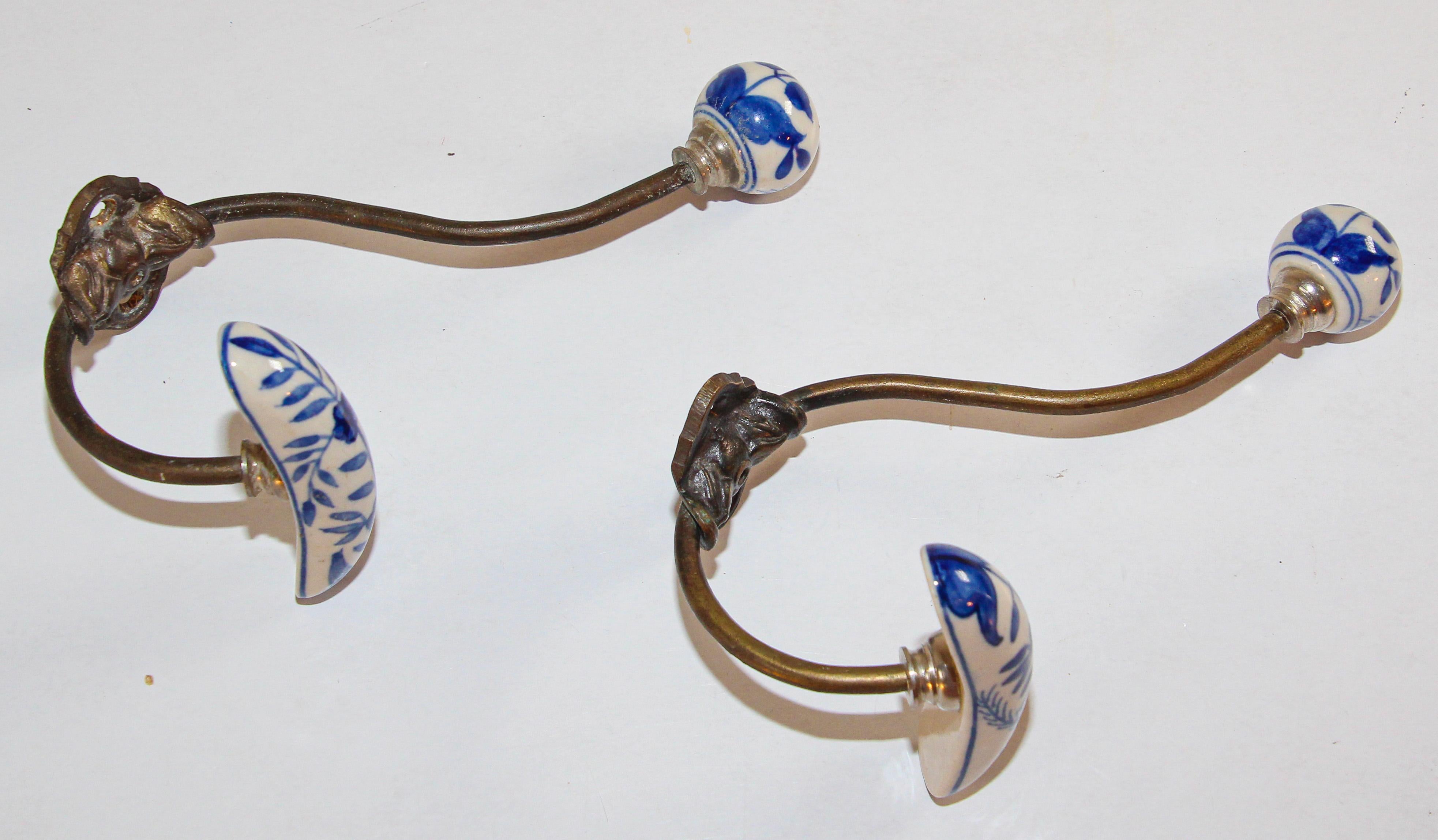 Vintage metal brass coat double hook with porcelain finals in blue and white Dutch Delft style floral design.
 This has a horizontal shaped bar which slopes downwards and is for hanging clothes, hats etc.
The hook is fastened to a shaped cartouche