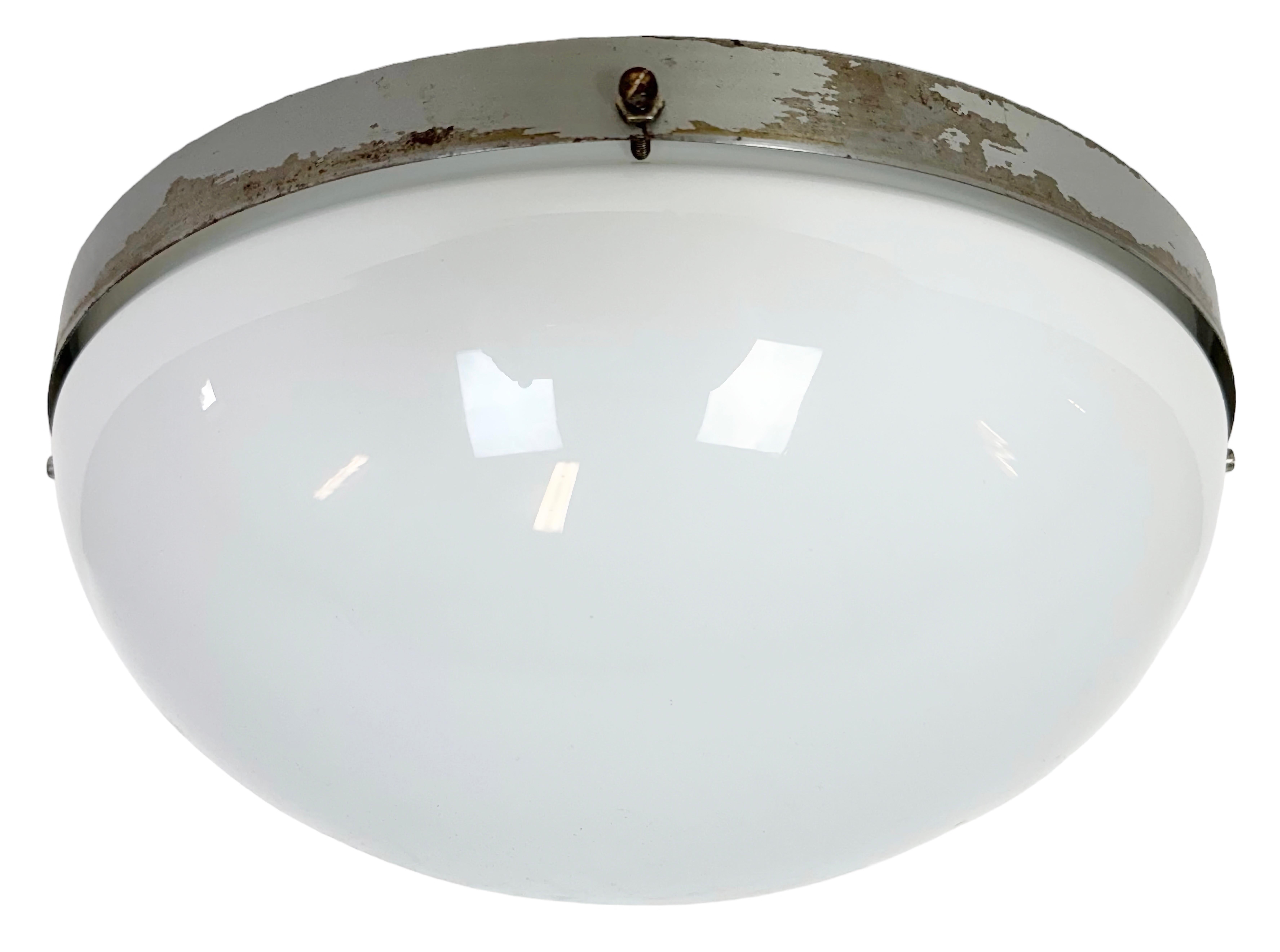 Vintage Industrial wall or ceiling lamp made by NAPAKO in former Czechoslovakia during the 1960s. Was used in factory offices and corridors. It features a grey metal back and a milk glass cover. The porcelain socket requires standard E 27/ E26 light