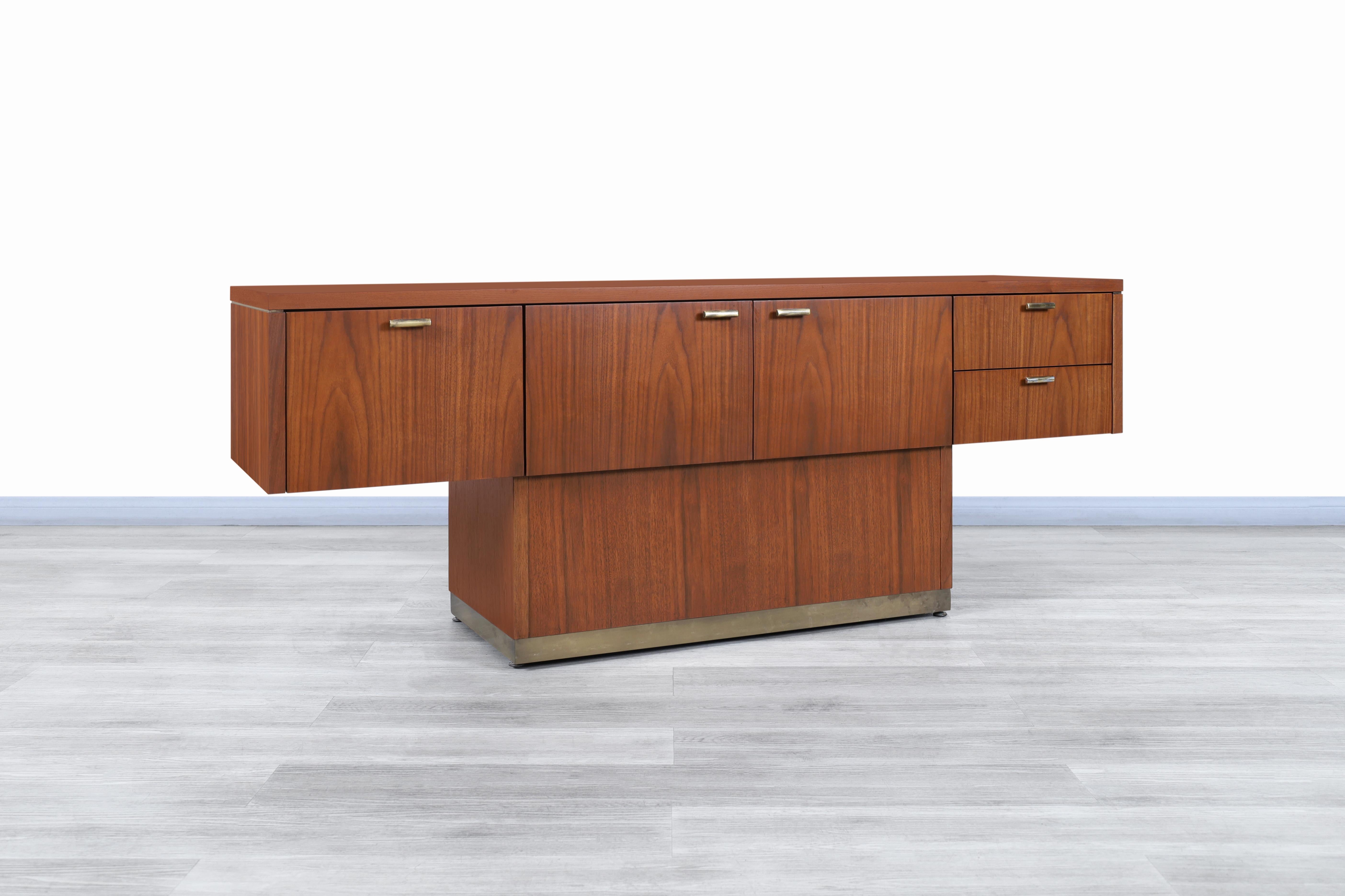 Wonderful vintage walnut and brass cantilevered credenza designed by Myrtle Desk Co. in the United States, circa 1970s. This desk features a cantilevered design supported by a pedestal base with solid brass accents. The desk has been built from