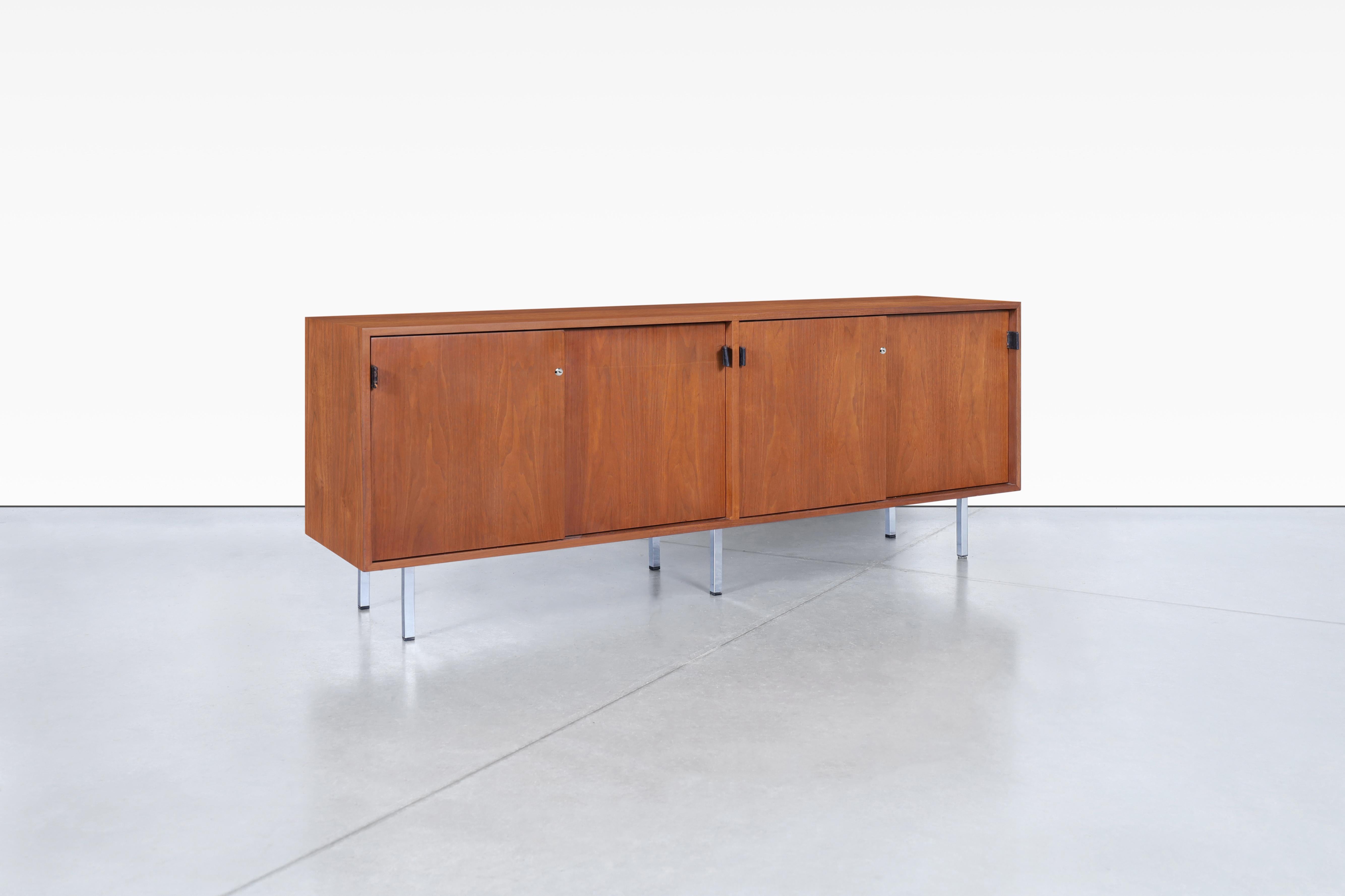 Introducing the stunning mid-century walnut credenza designed by architect and furniture designer Florence Knoll for Knoll Associates Inc. This iconic piece boasts four sliding doors, each adorned with original black leather handles that have