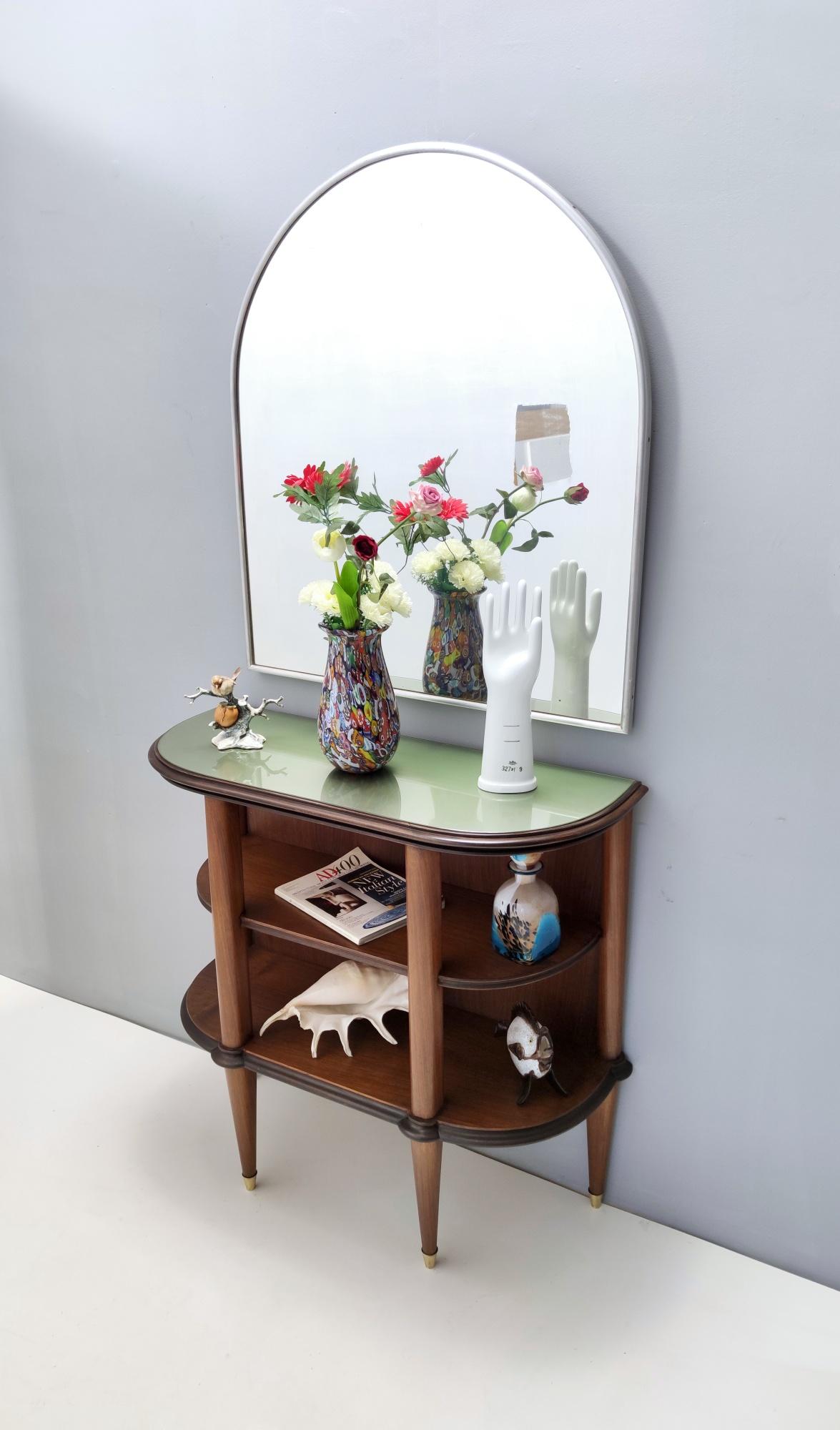 Made in Italy, 1940s - 1950s. 
This console table is made in walnut and moulded ebonized beech edges and features a demilune back-painted glass top and brass feet caps. 
It is a vintage item, therefore it might show slight traces of use, but it can