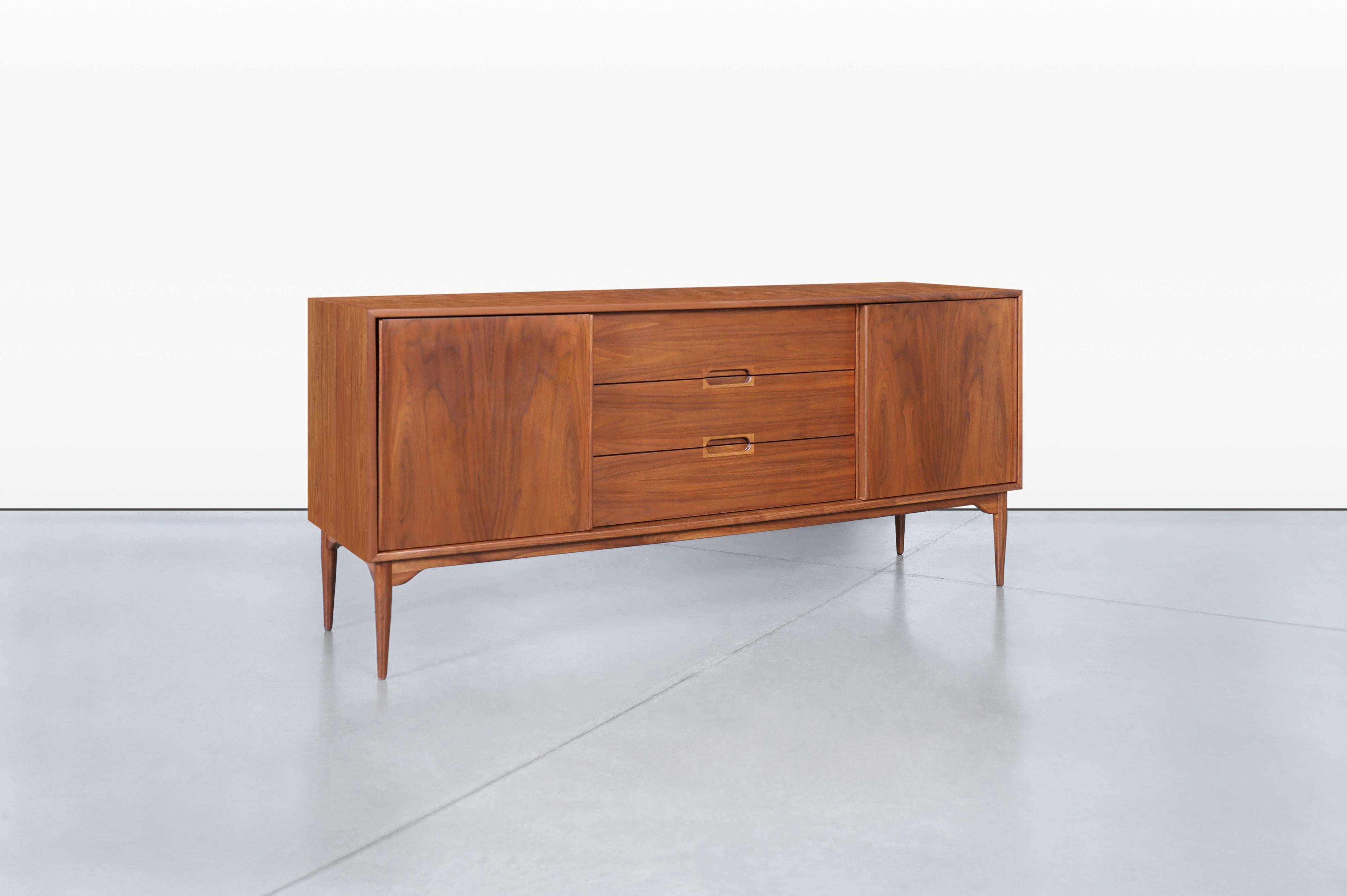 An exquisite mid-century modern walnut credenza, expertly designed by John Keal for Brown Saltman in the United States during the iconic 1950s. This piece combines form and function seamlessly, featuring three elegantly dovetailed drawers and two