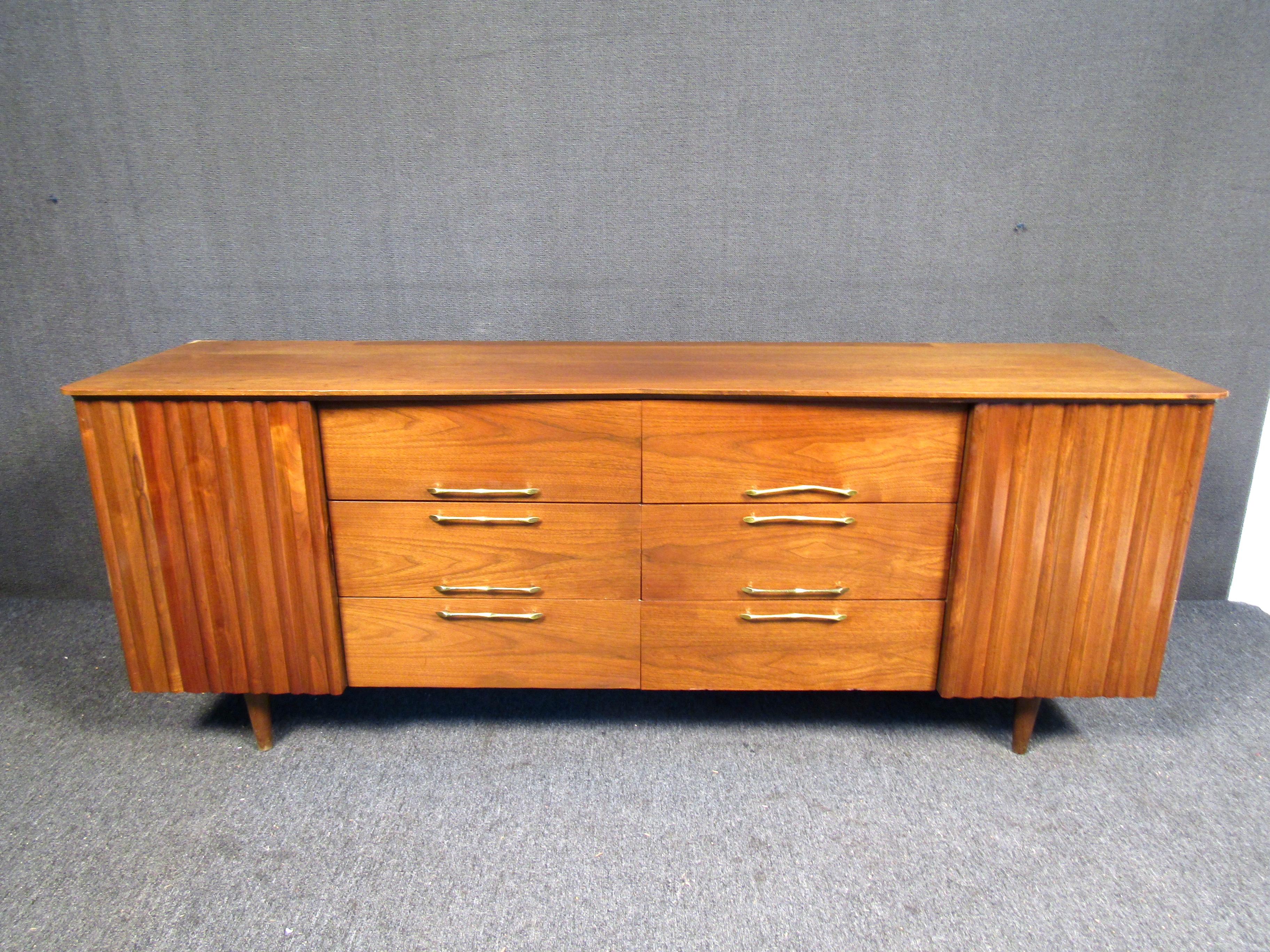This odd walnut credenza features twelve drawers with doors that cover three per side, it also has sleek brass handles that add pop to the overall beauty of the piece. Please confirm item location (NJ or NY).
