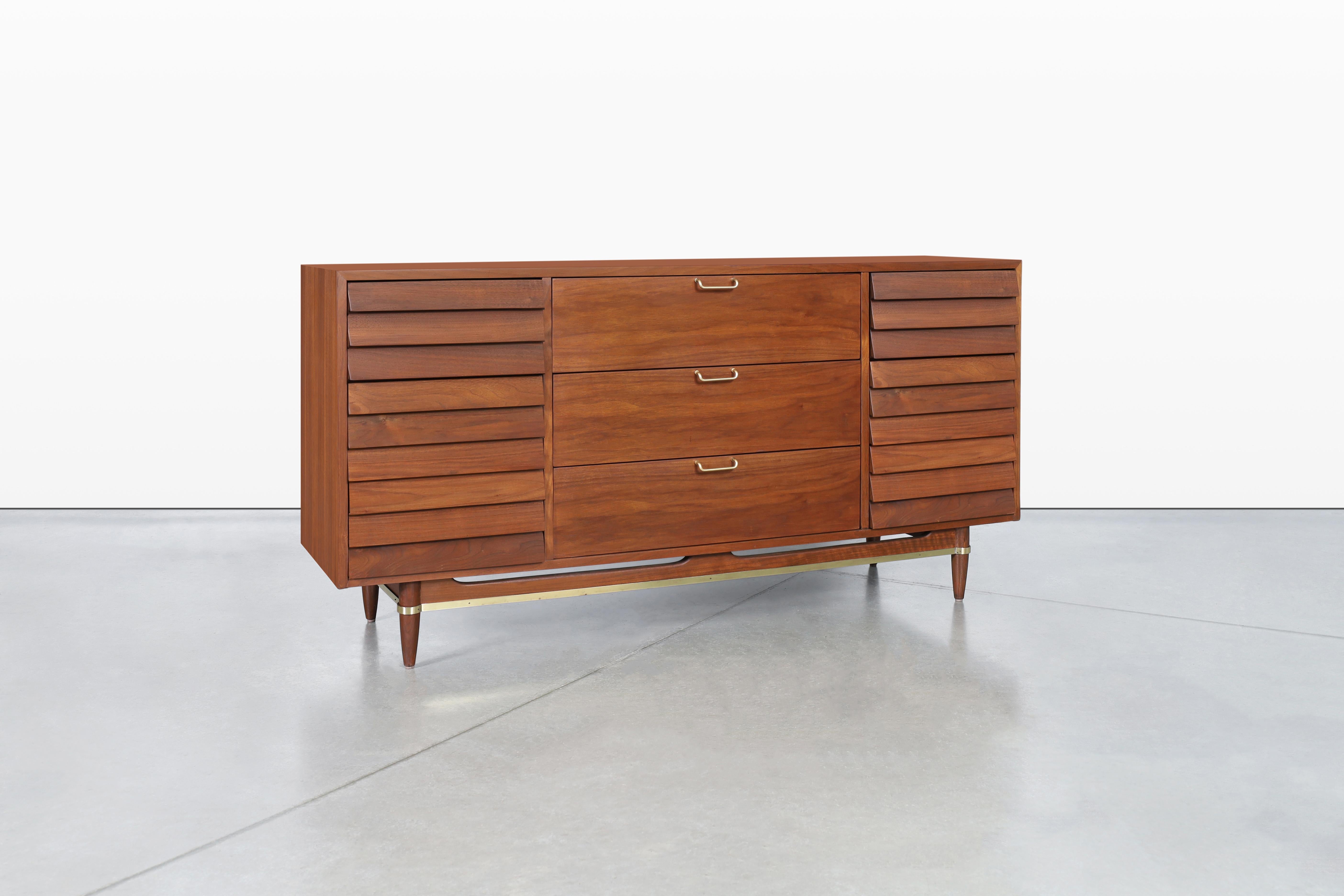 Preciosa cómoda de nogal moderna de mediados de siglo, fabricada con maestría por Merton L. Gershun para American of Martinsville en la década de 1960. Esta pieza muestra una caja de nogal bellamente diseñada que se alza con gracia sobre una base
