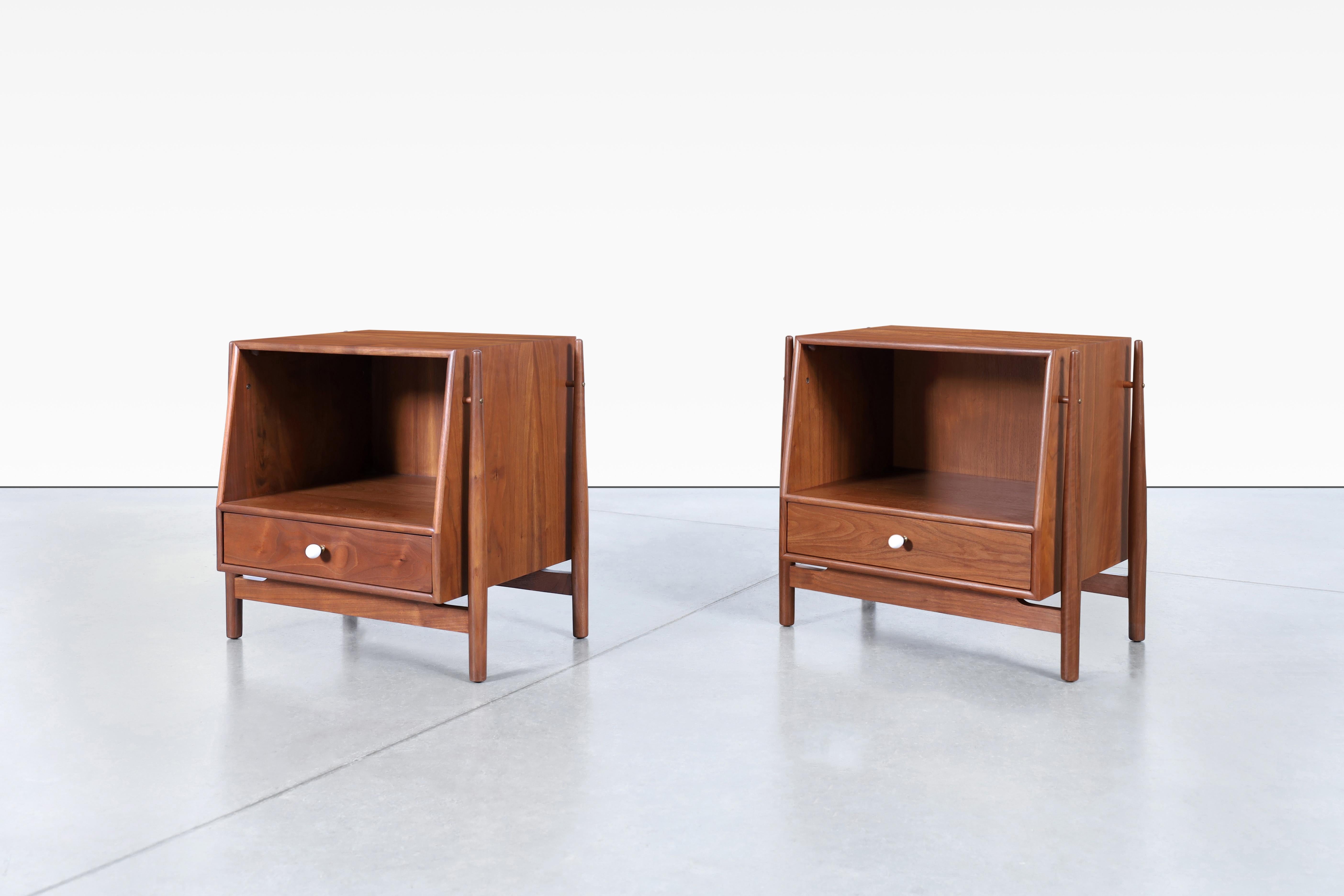 These mid-century walnut nightstands were designed by Kipp Stewart and Stewart McDougall for Drexel in the 1950s as part of the Declaration Line. Each nightstand features a large cubby and a single dovetail drawer with its original porcelain pull.