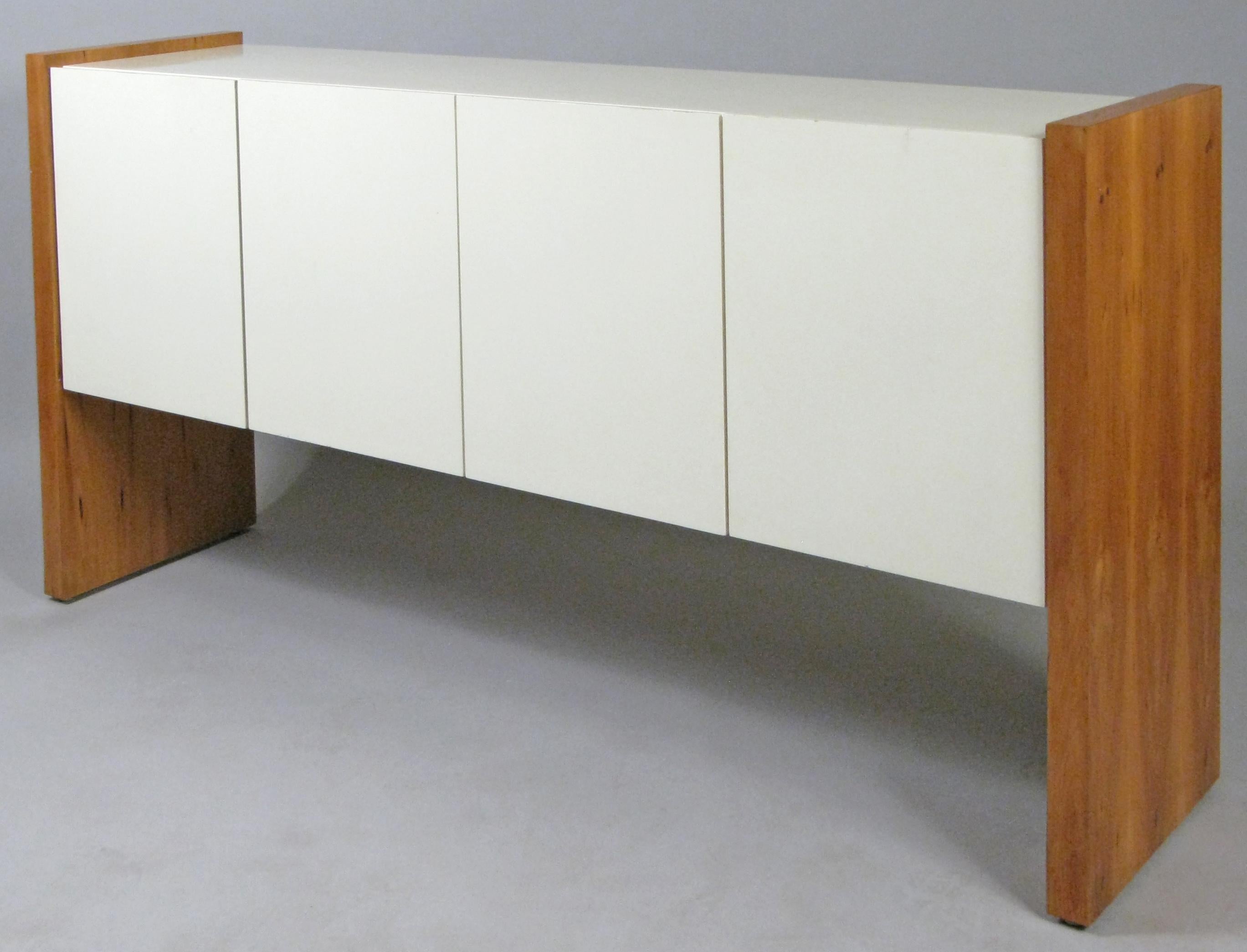 A very handsome and iconic 1960s cabinet designed by Milo Baughman for Thayer Coggin. designed with an ivory lacquered cabinet 'floating' between the two walnut bases. the cabinet has two pairs of hinged doors, the left one for an adjustable shelf