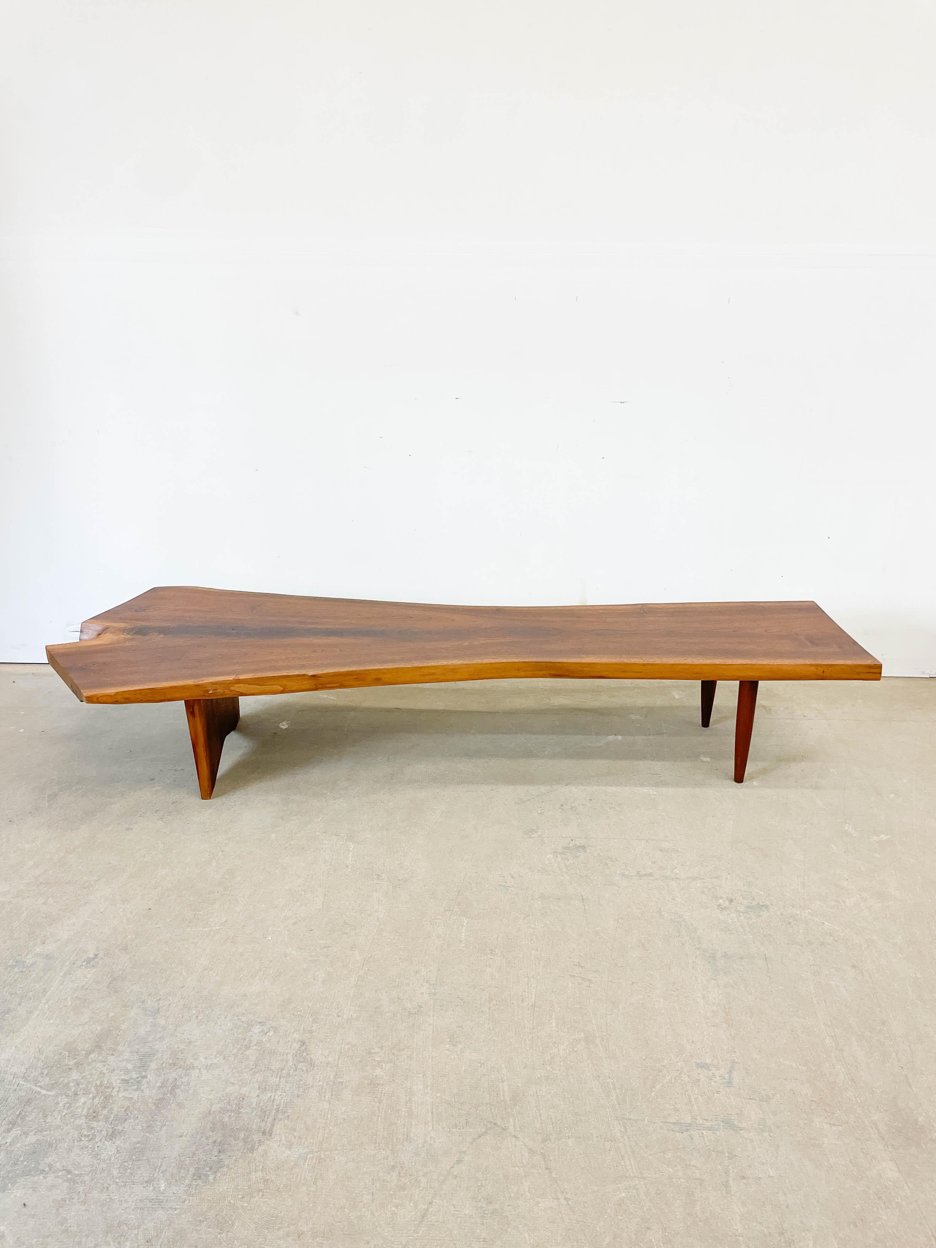 Bellissima panca o tavolino di grandi dimensioni con bordo vivo nello stile di George Nakashima. La splendida venatura del legno di noce, i bordi vivi su entrambi i lati e i dettagli aggraziati della base ispirata a Wood Wood ne fanno un pezzo di