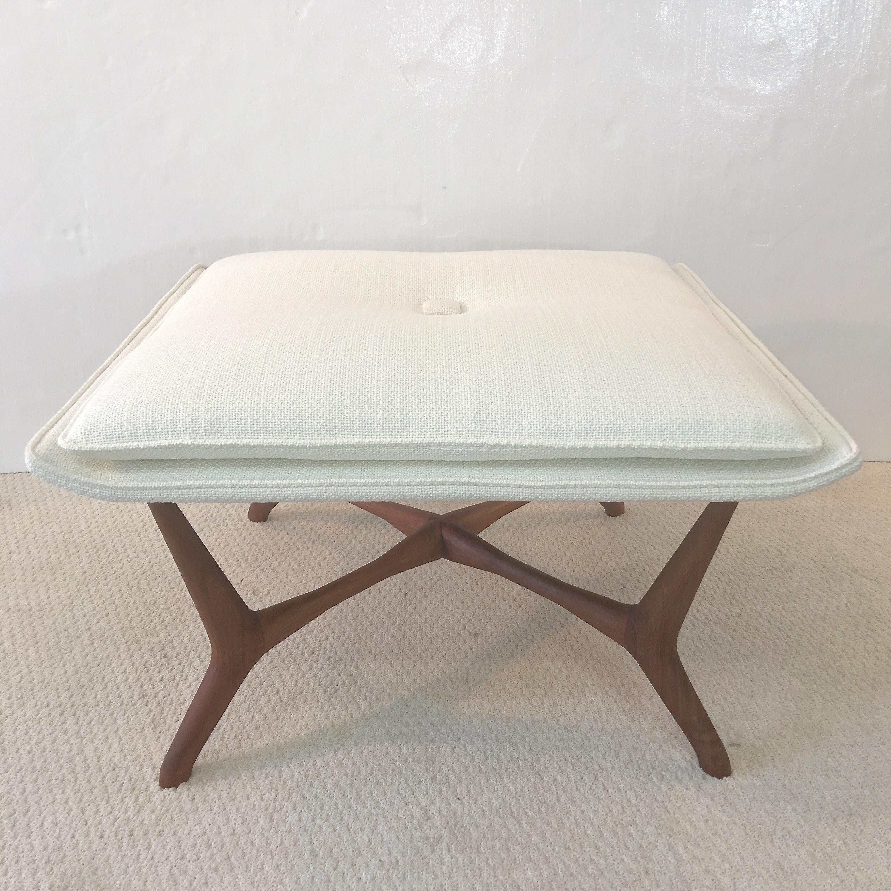 A low square ottoman; sculpted solid walnut splayed leg base, square top with two up-curved sides, freshly upholstered in ivory woven cotton/rayon with matching loose square pillow cushion. Vintage late 1950s. 