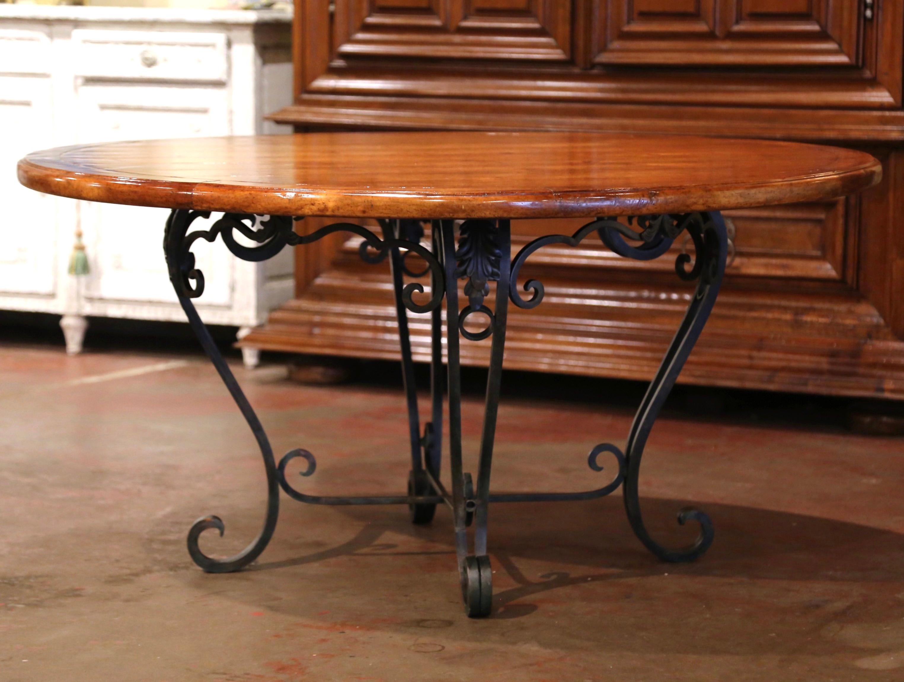 Crafted in the USA circa 1990, the elegant table stands on forged cabriole legs ending with scrolled feet over a curved bottom stretcher. The circular wooden top features old timber planks set inside a round frame over an intricate scalloped apron
