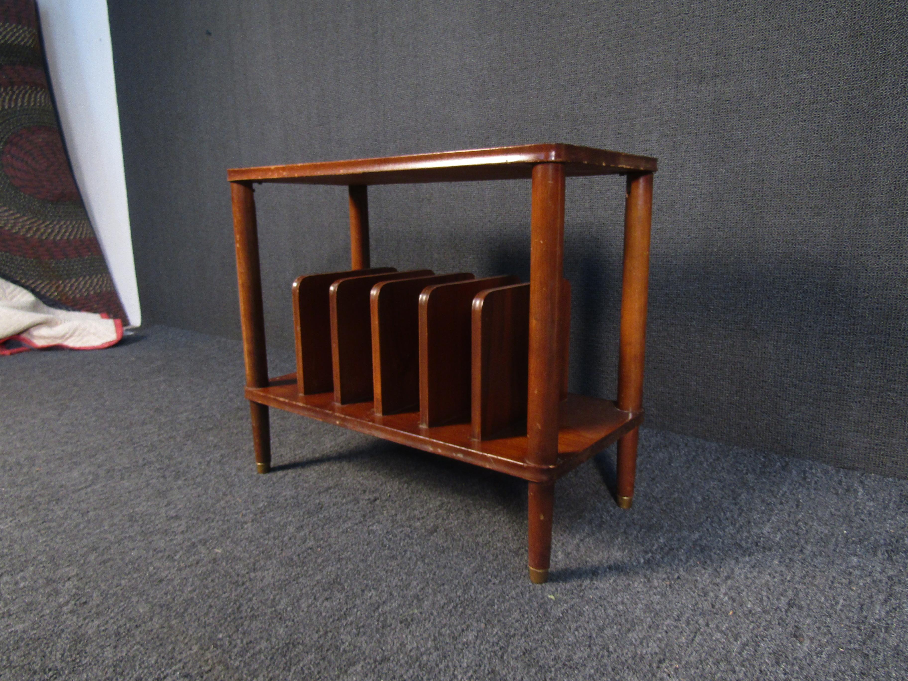 With rich walnut woodgrain and brass footing, this side table offers plenty of classic Mid-Century Modern style. The lower tier of the table holds a magazine rack, making this side table perfect for a living room or reading room. Please confirm item